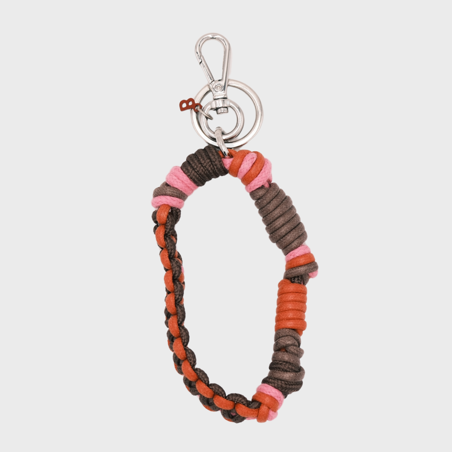 A woven macramé key chain with red, brown and pink patterns, inspired by Celtic knots, finished with silver-tone metal hardware.