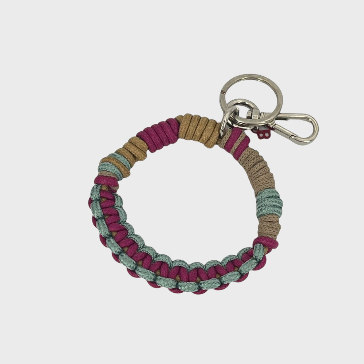 A woven macramé key chain with beige, pink, brown and light green patterns, inspired by celtic knots, finished with silver-tone metal hardware.