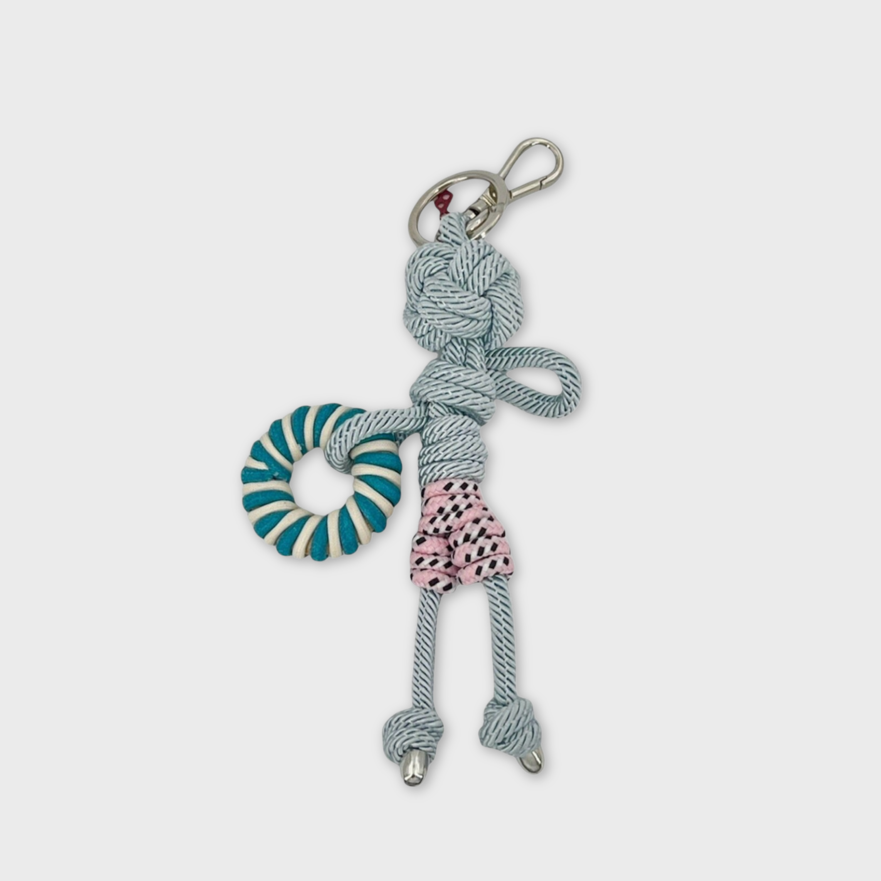 Handmade blue macramé bag charm featuring a male character, meant to be at the beach, wearing striped pink and white swimming shorts and holding a pool float. He is attached to a silver clasp.