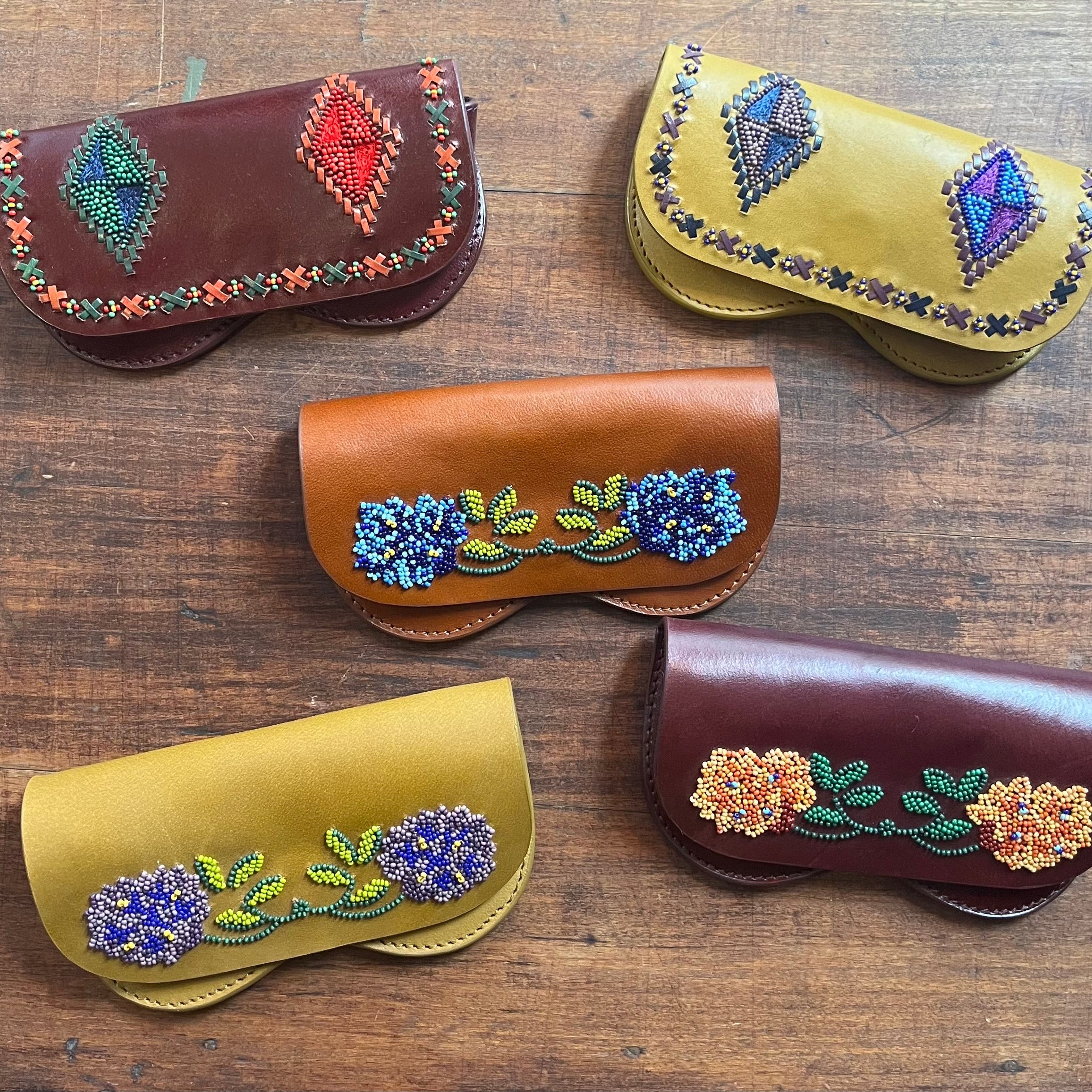 Four leather glasses cases with colorful beaded floral and geometric designs, including the yellow cherokee one. 