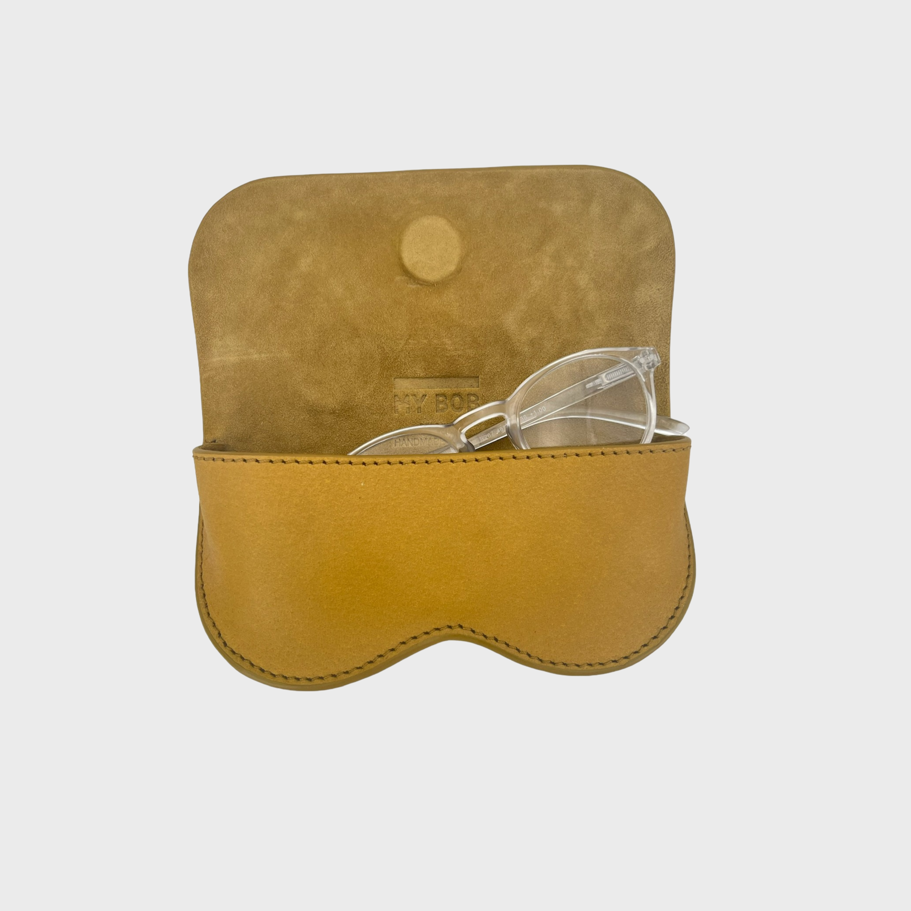 A yellow mustard leather glasses case shown open on a light gray background, with clear-framed eyeglasses resting inside the lower compartment.