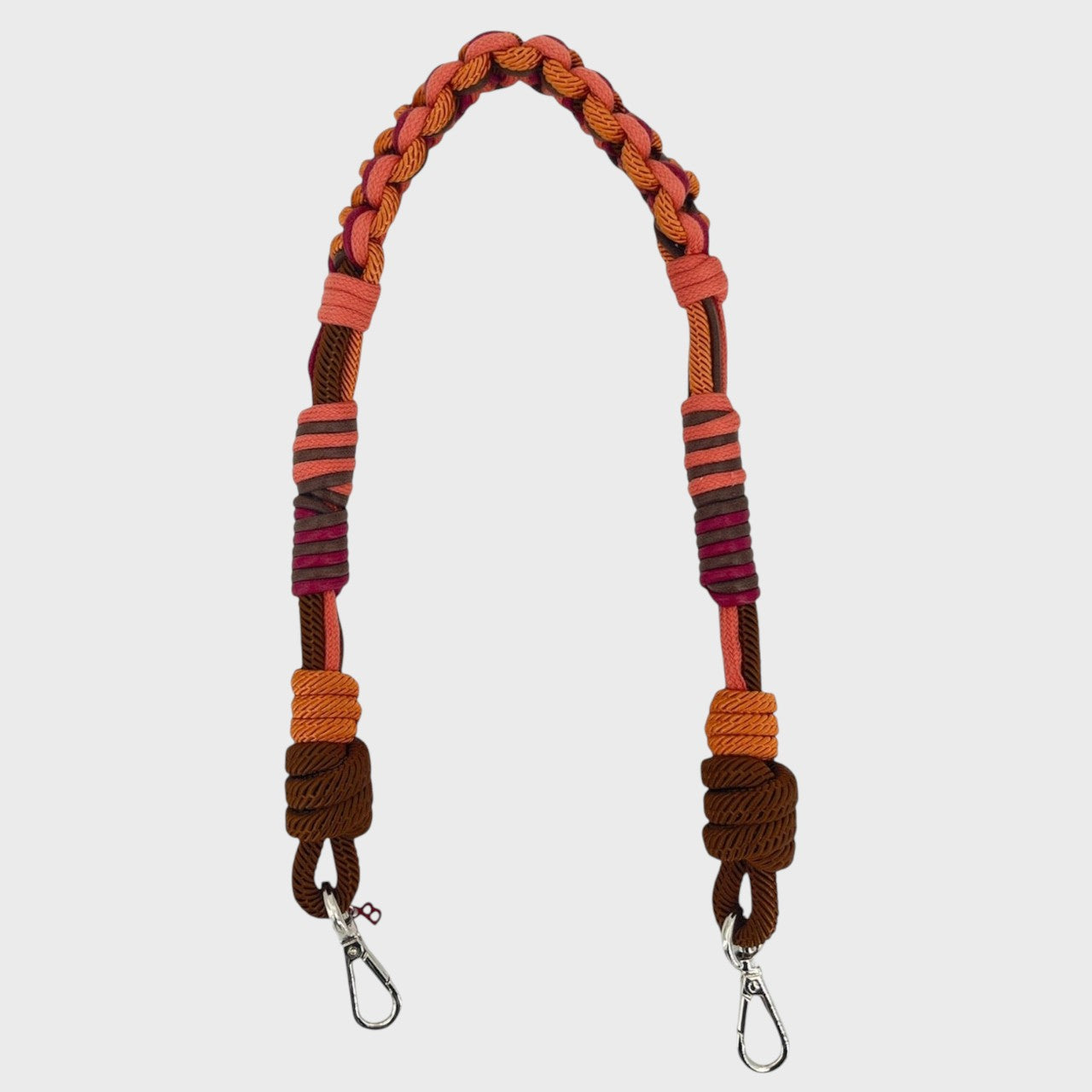 Multicolored braided macramé bag strap in orange, dark brown, and red, shown on a light gray background.