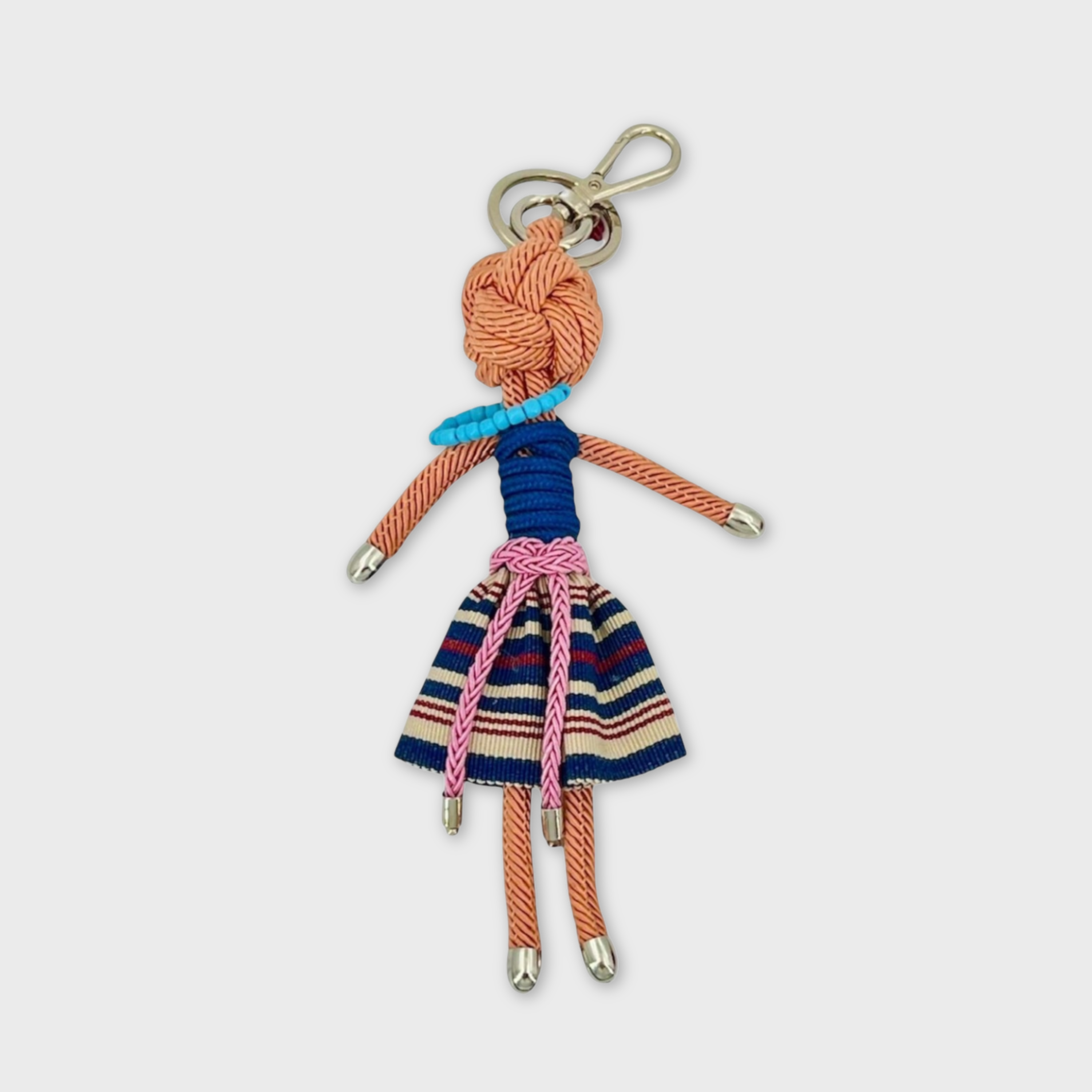 Bag charm featuring a character in a blue, beige and red striped mini skirt, a dark blue top and a pink knotted belt. She is wearing a blue beaded necklace and is attached to a silver clasp. 