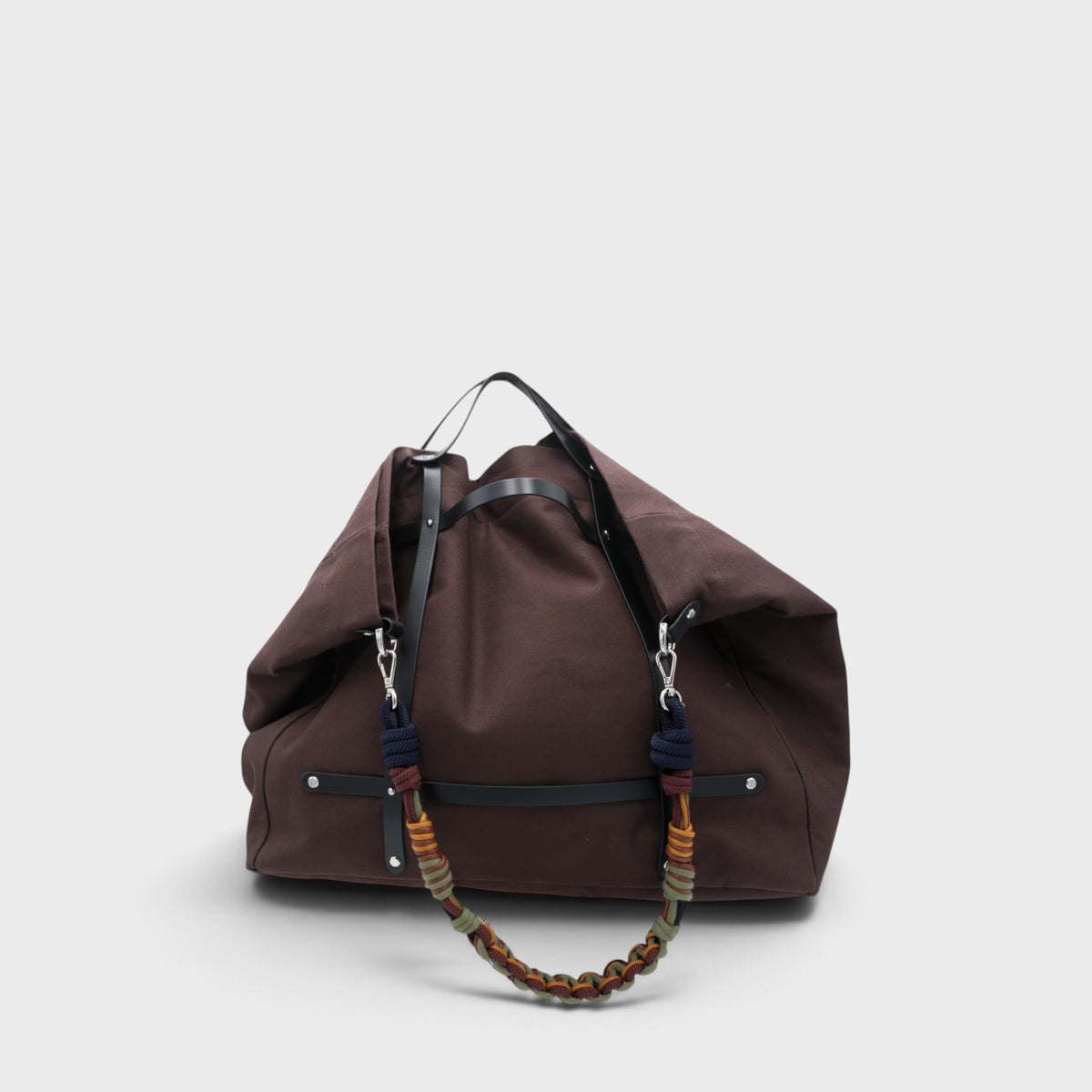 Model carrying a chcolate canvas weekend or duffle bag with a black leather harness, paired with a neutral toned shoulder strap in yellow, green and brown.