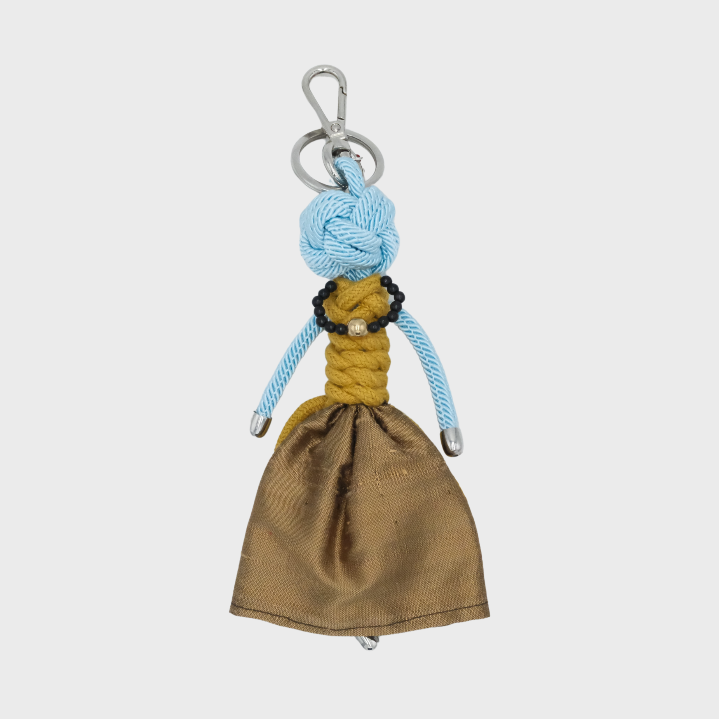 A handmade keychain doll with a light blue knotted rope head, yellow braided rope torso, and a brown fabric skirt, attached to a silver metal key ring.