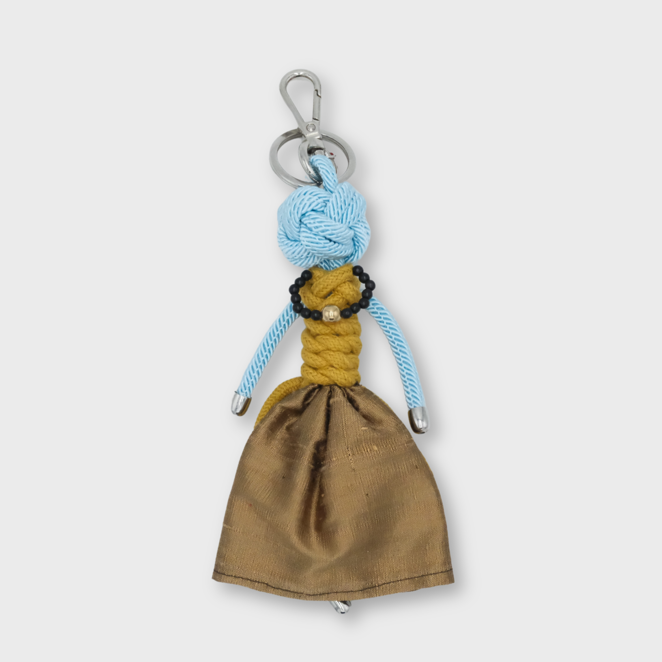 A handmade keychain doll with a light blue knotted rope head, yellow braided rope torso, and a brown fabric skirt, attached to a silver metal key ring.