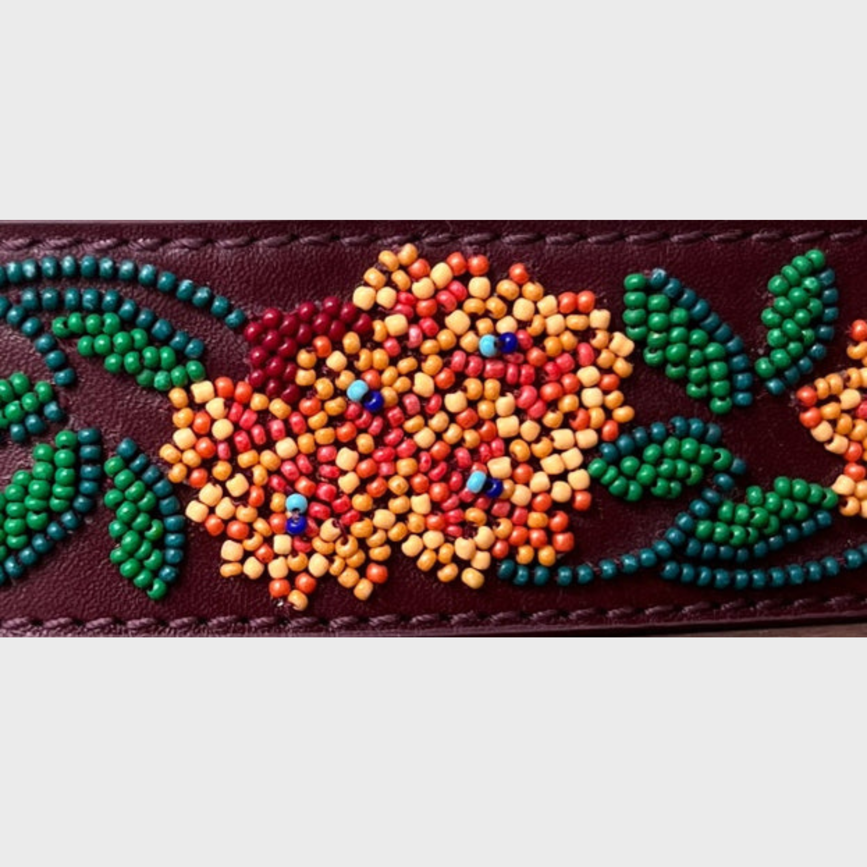 A close-up of a dark brown leather belt featuring colorful beaded floral patterns with green leaves, orange and yellow petals, and small blue accents.