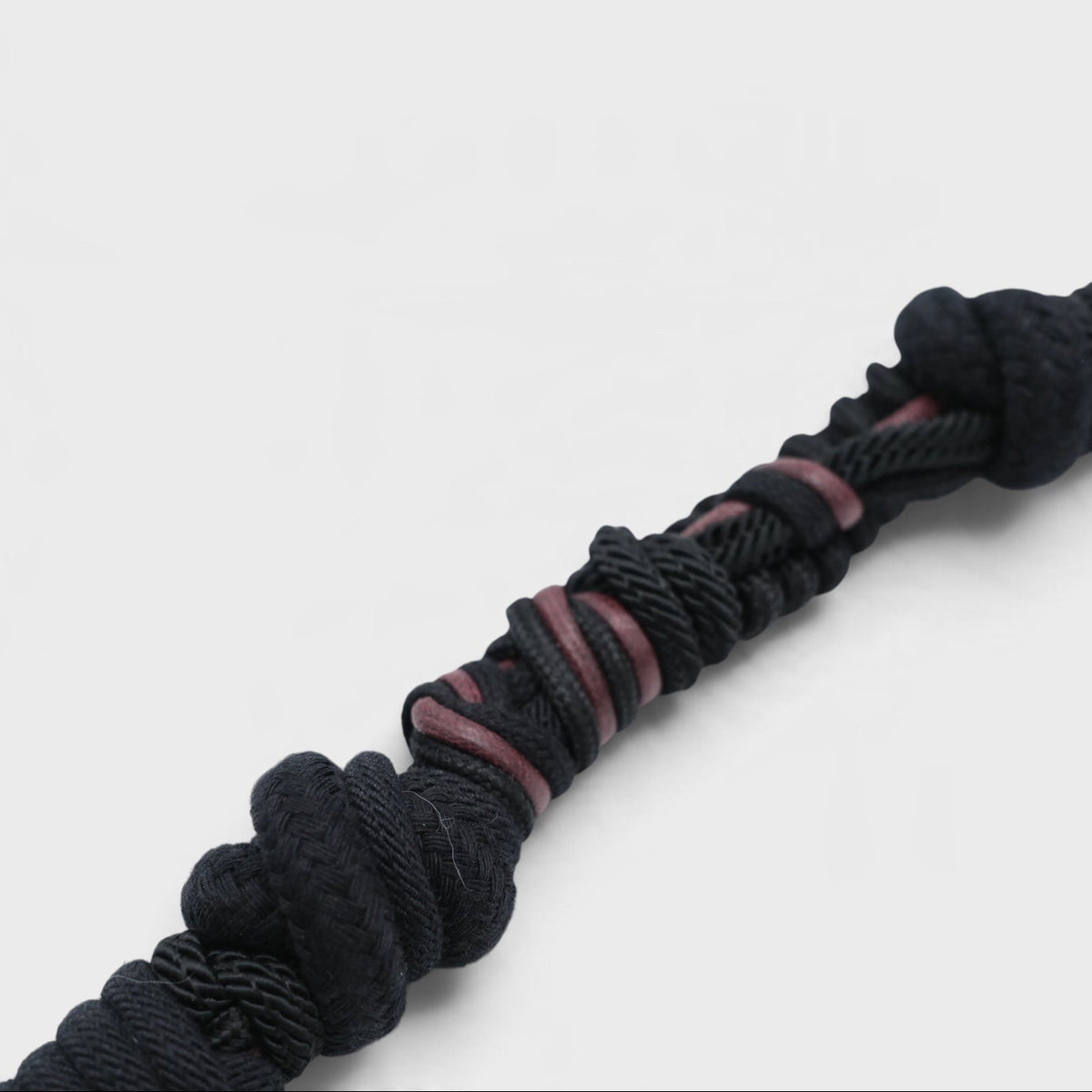 A close-up of a thick black braided rmacrame bag strap with a knotted end, showing thin dark brown inner strands, set against a plain light gray background.