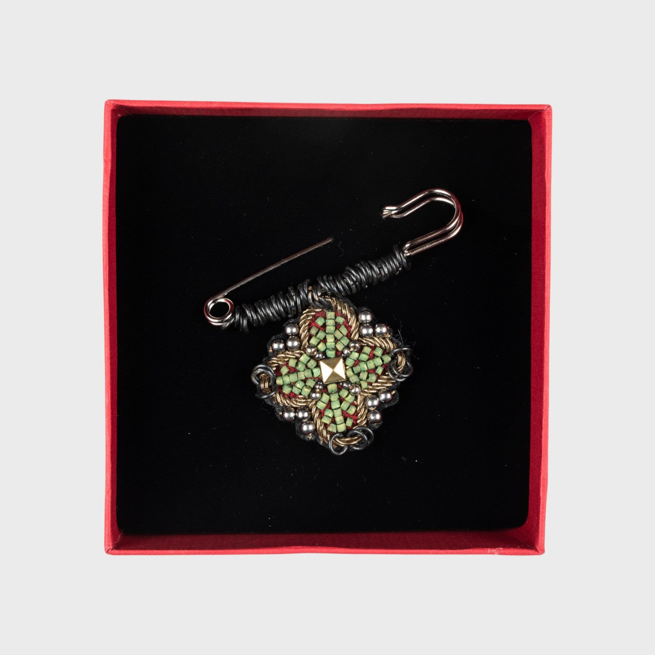 An embroidered pin with green details in a box. 