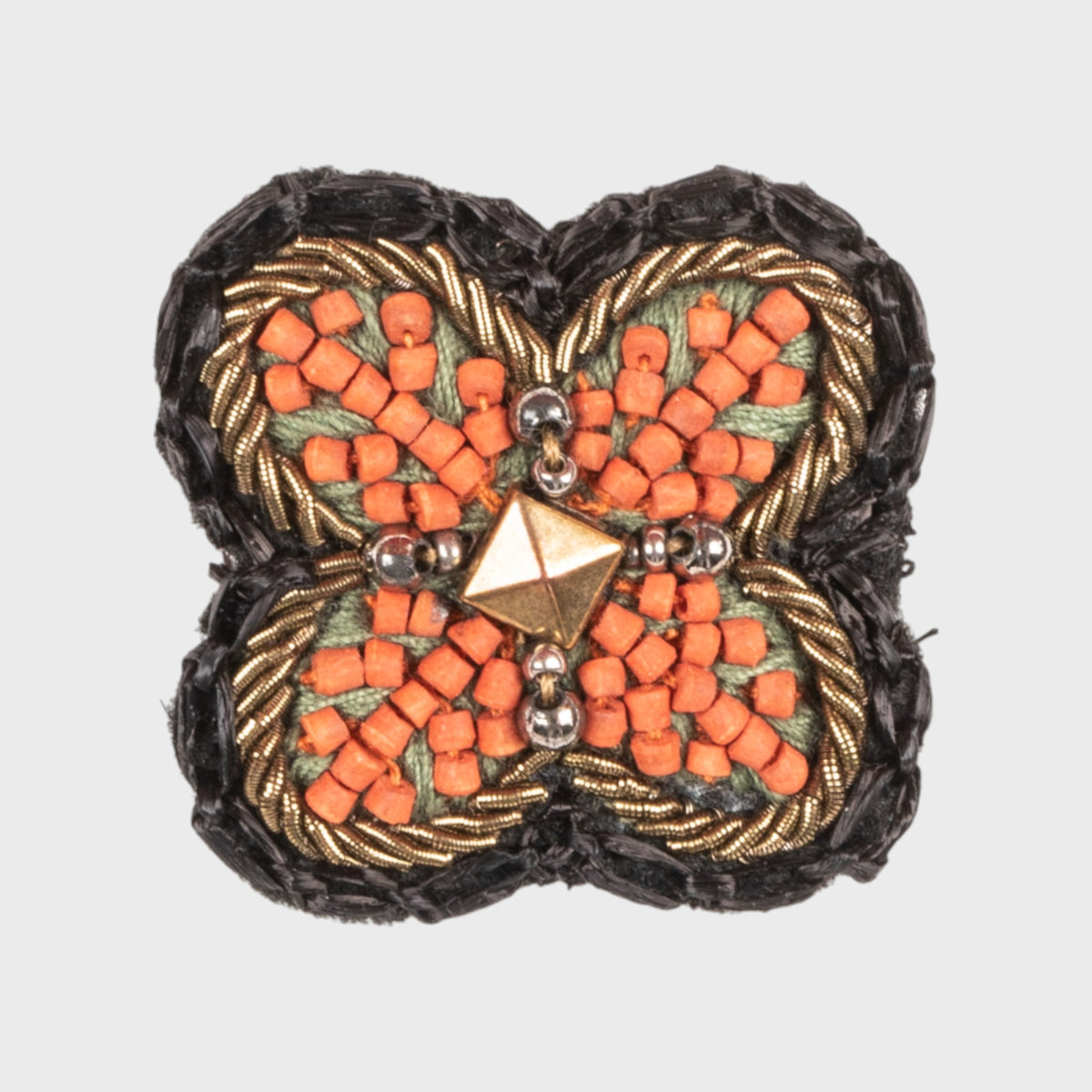 Decorative embroidered brooch with orange and gold pattern on a white background