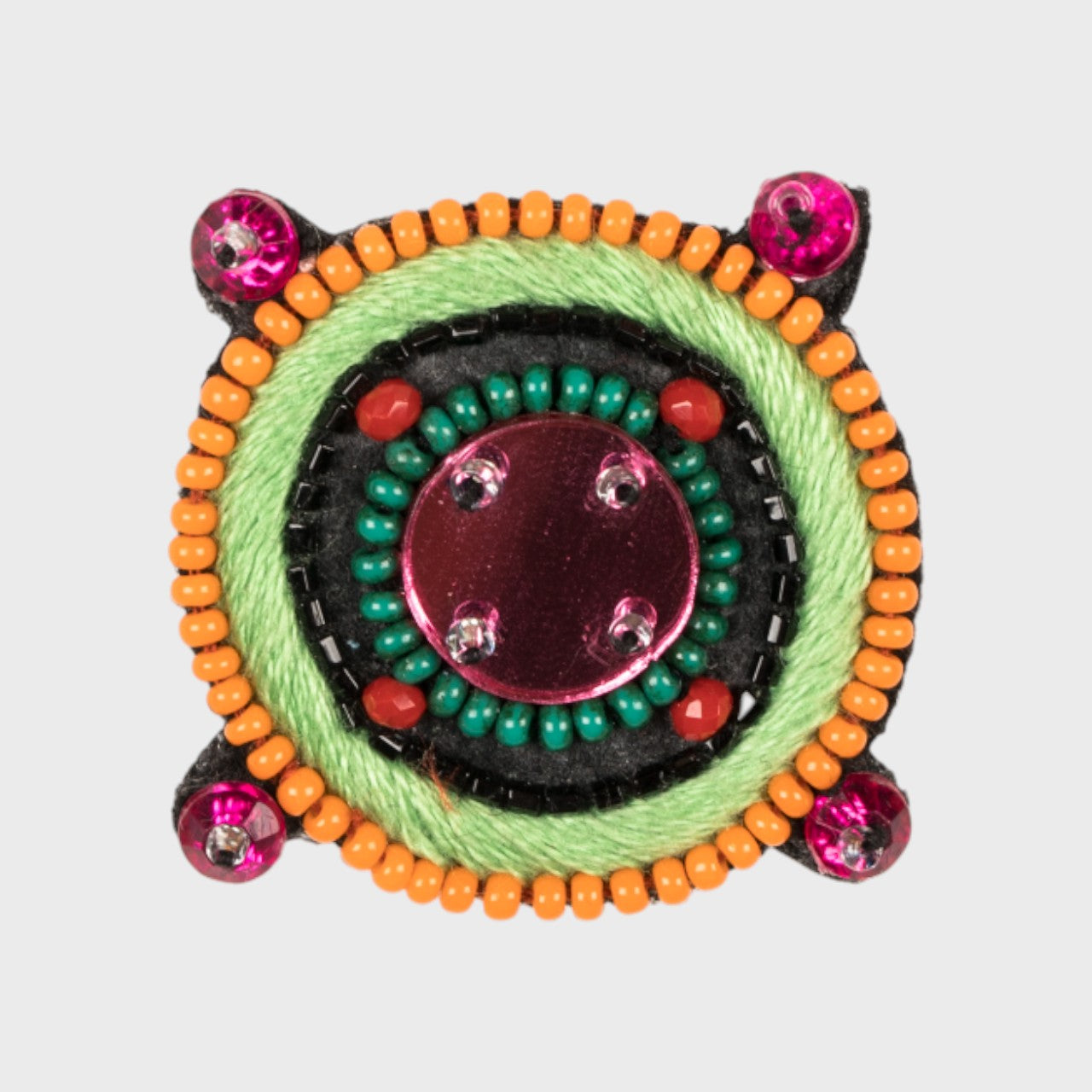 An embroidered brooch representing a compass with a pink glass stoned middle and orange and green details. 