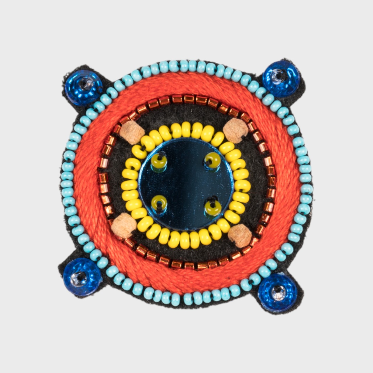 An embroidered brooch representing a compass with a blue glass stoned middle and red, yellow and blue details. 