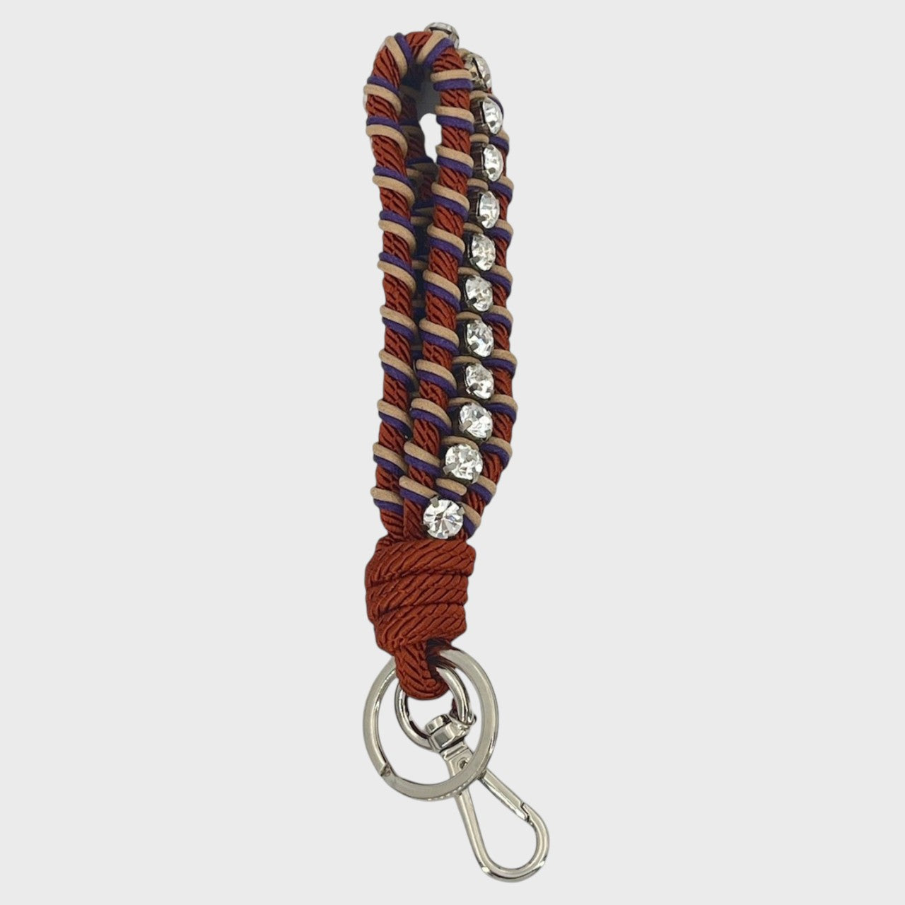 A macramé braided keychain strap featuring a copper, beige and purple pattern, accented with a vertical row of silver rhinestones, and finished with a silver metal lobster clasp on a light gray background.