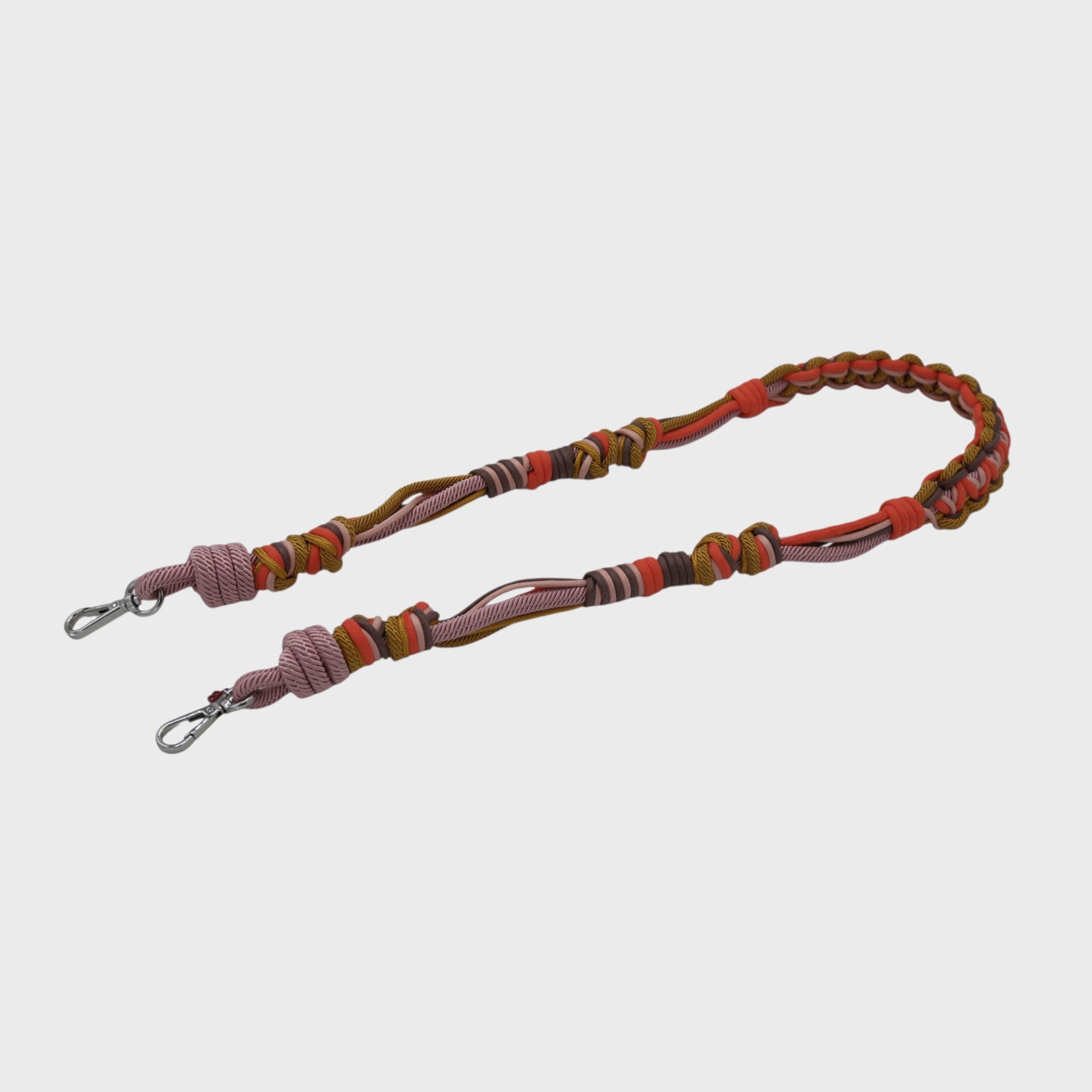 Multicolored braided macramé bag strap in orange, soft pink, and soft yellow with metal hooks on a light gray background.