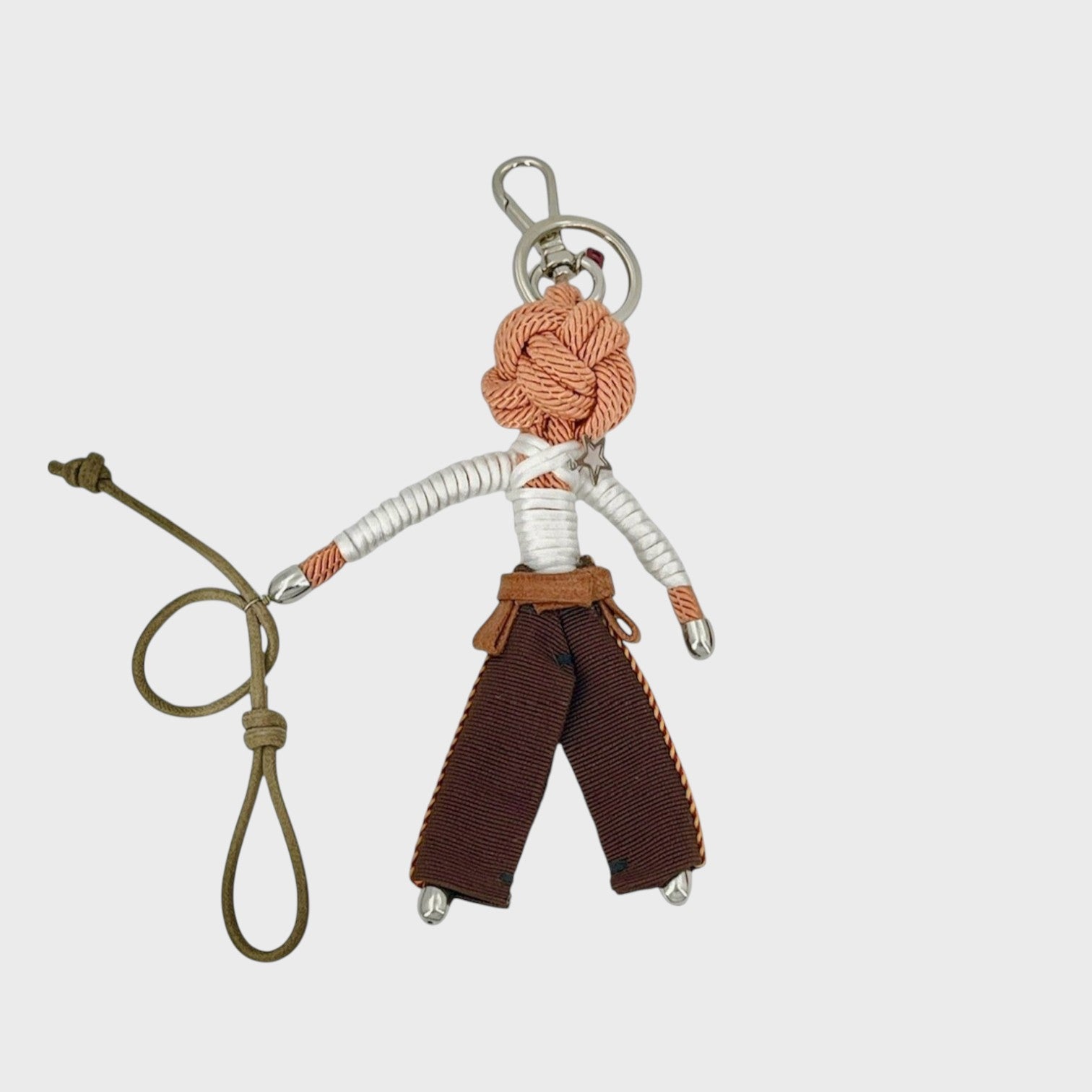 Handmade tan macramé bag charm featuring a male character, meant to be a cowboy with his lasso, wearing traditional brown cowboy trousers, a belt and a long sleeves white top. He is attached to a silver clasp.