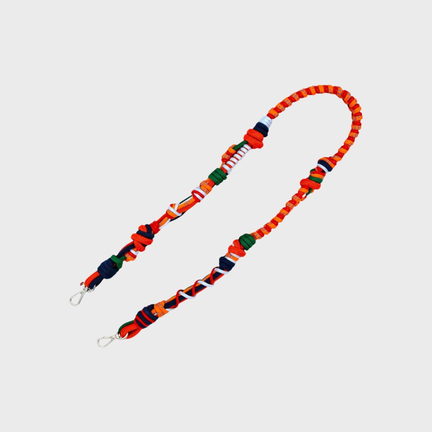 Multicolored braided macramé bag strap in bright and dark orange, dark green, and white, shown on a light gray background.
