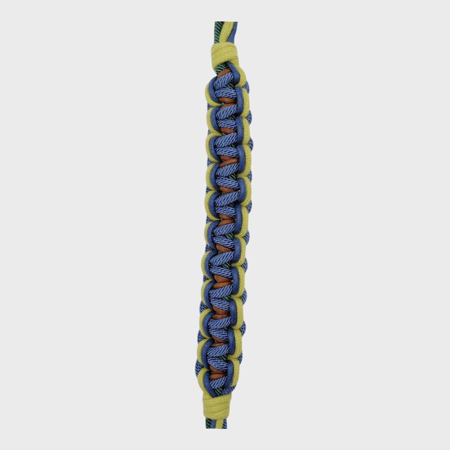 Close up of the multicolored braided macramé bag strap in bright and dark green, dark blue, and brown, shown on a light gray background.