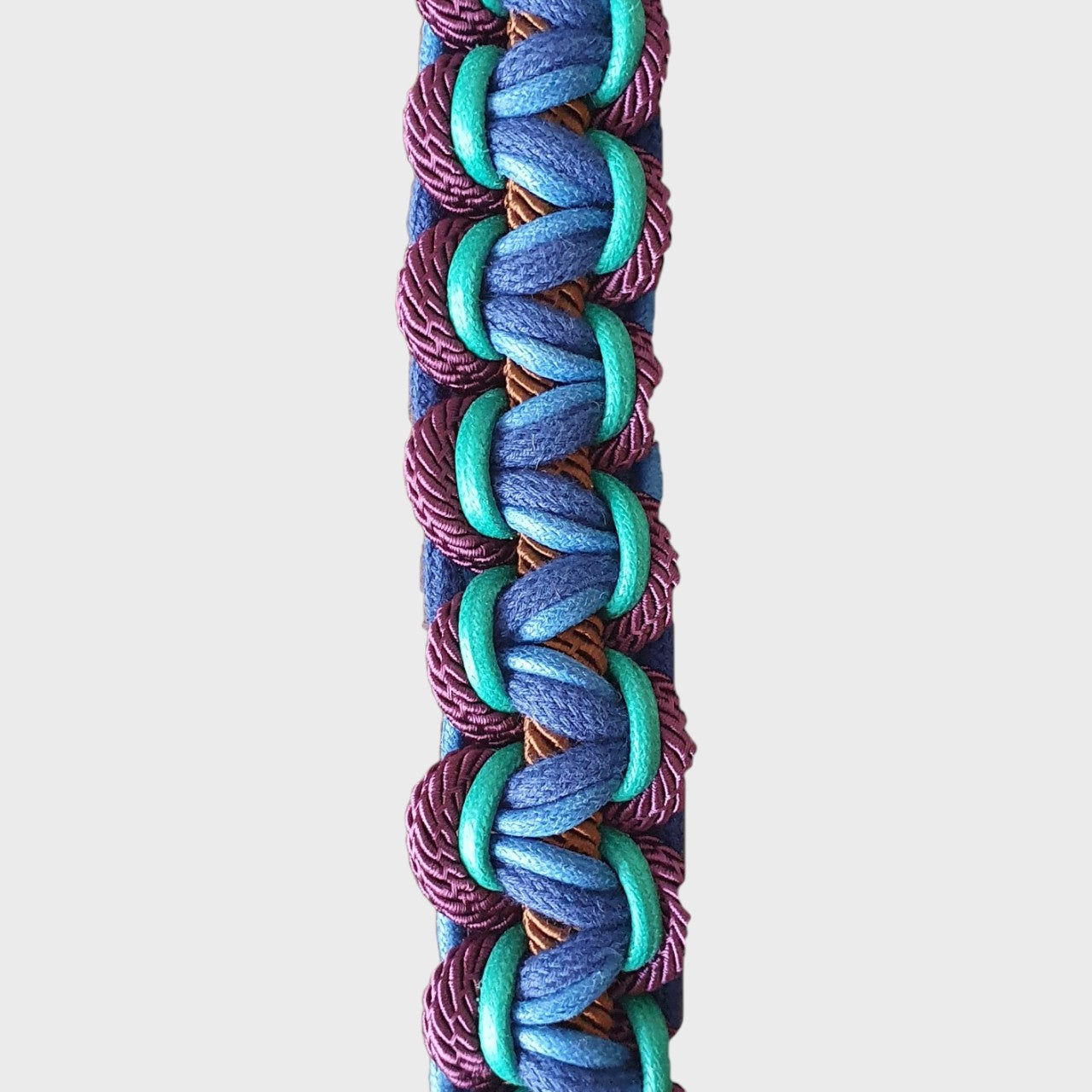 Close up of the multicolored braided macramé bag strap in various blues, with accents of purple and brown shown on a light gray background.