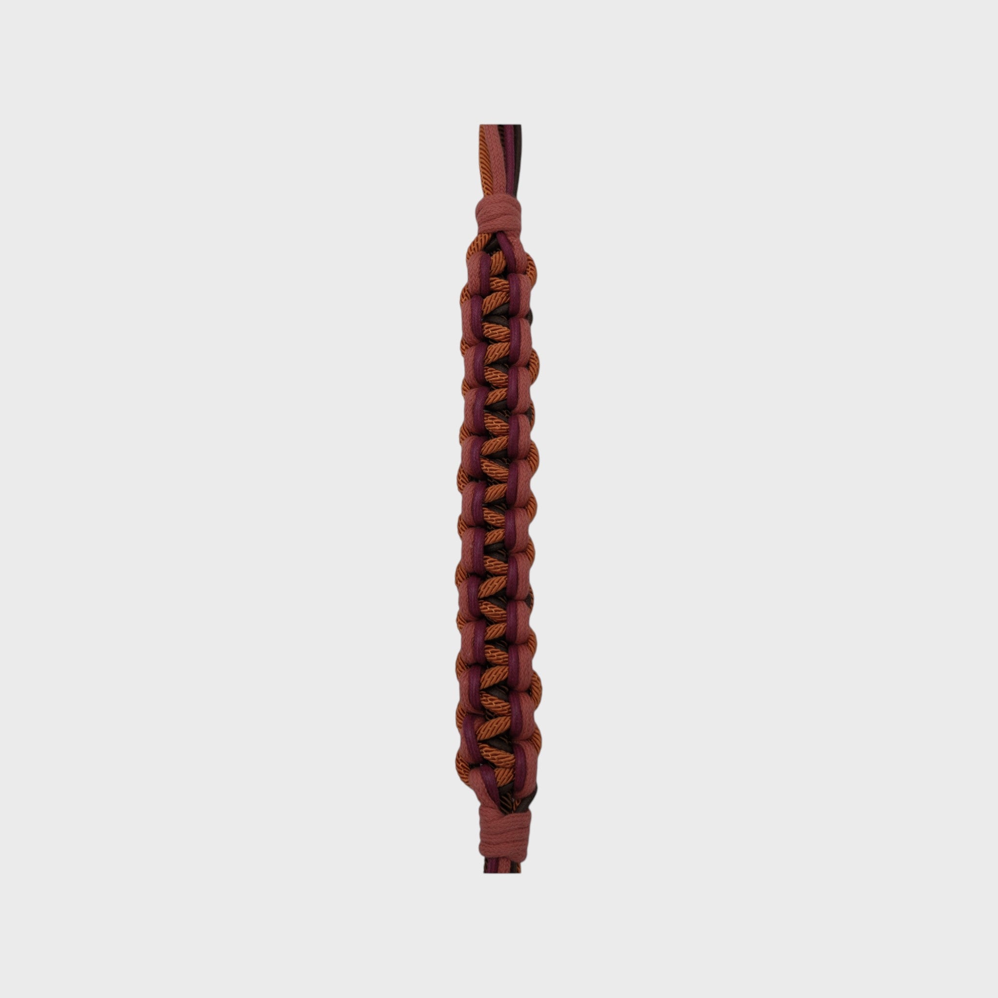 Close up of the multicolored braided macramé bag strap in orange, dark brown, and red, shown on a light gray background.