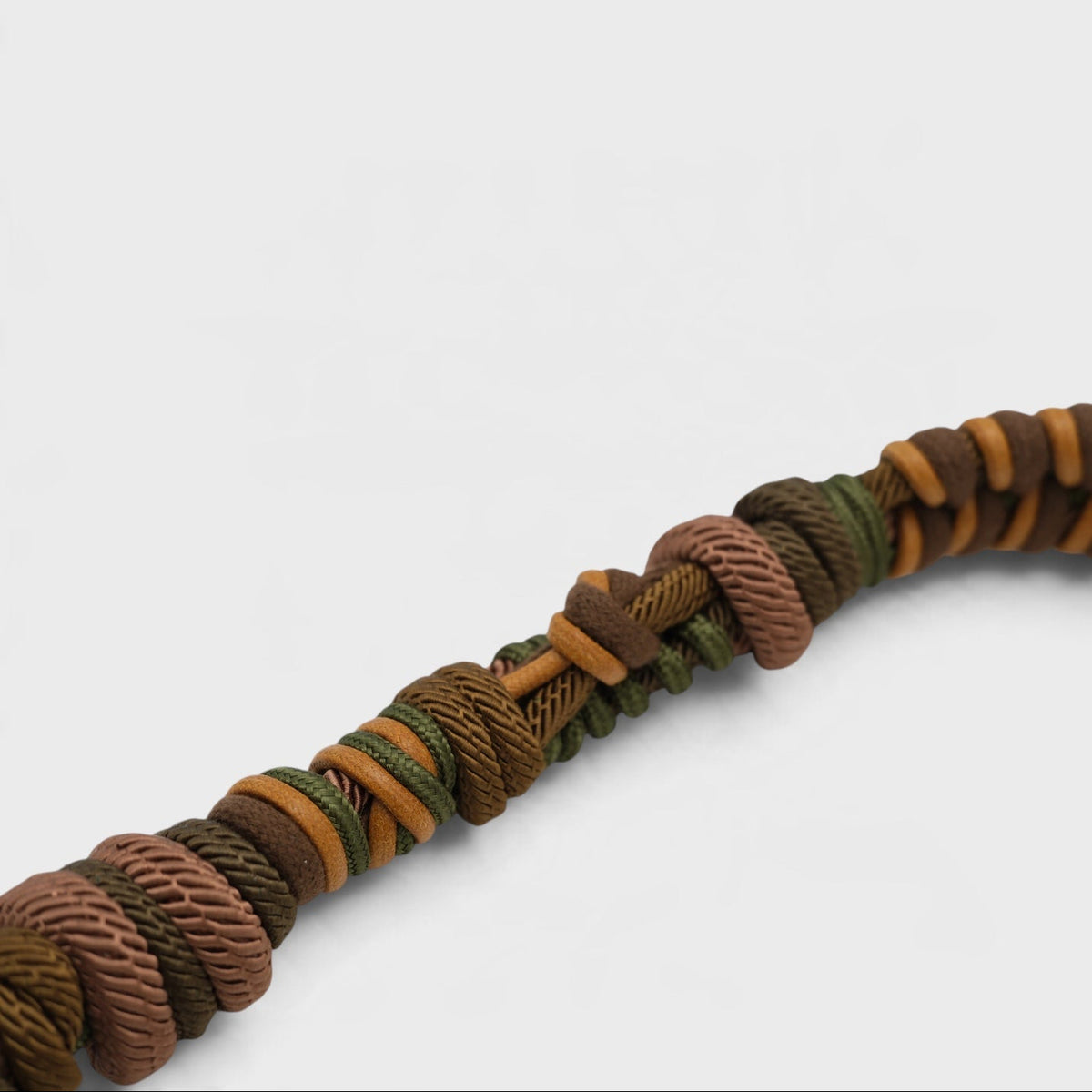 A close-up of a braided macramé bag strap, featuring a pattern of brown, olive green, and tan cords, set against a plain light gray background.