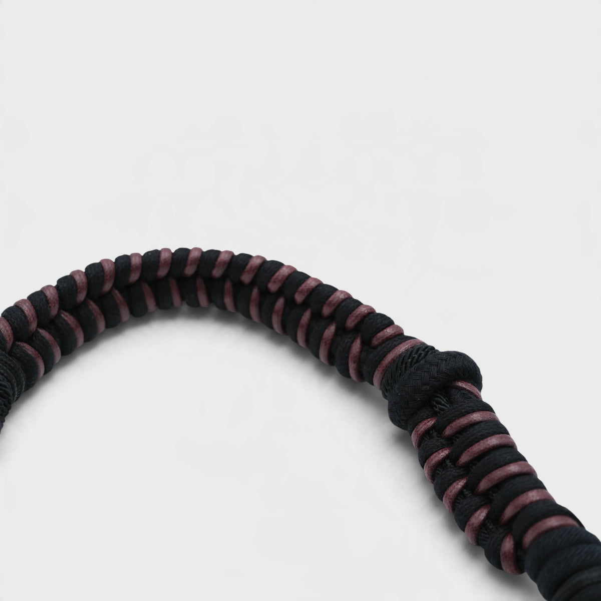 A close-up of a braided macrame bag strap with alternating dark brown and black stripes, photographed on a clean light gray background.