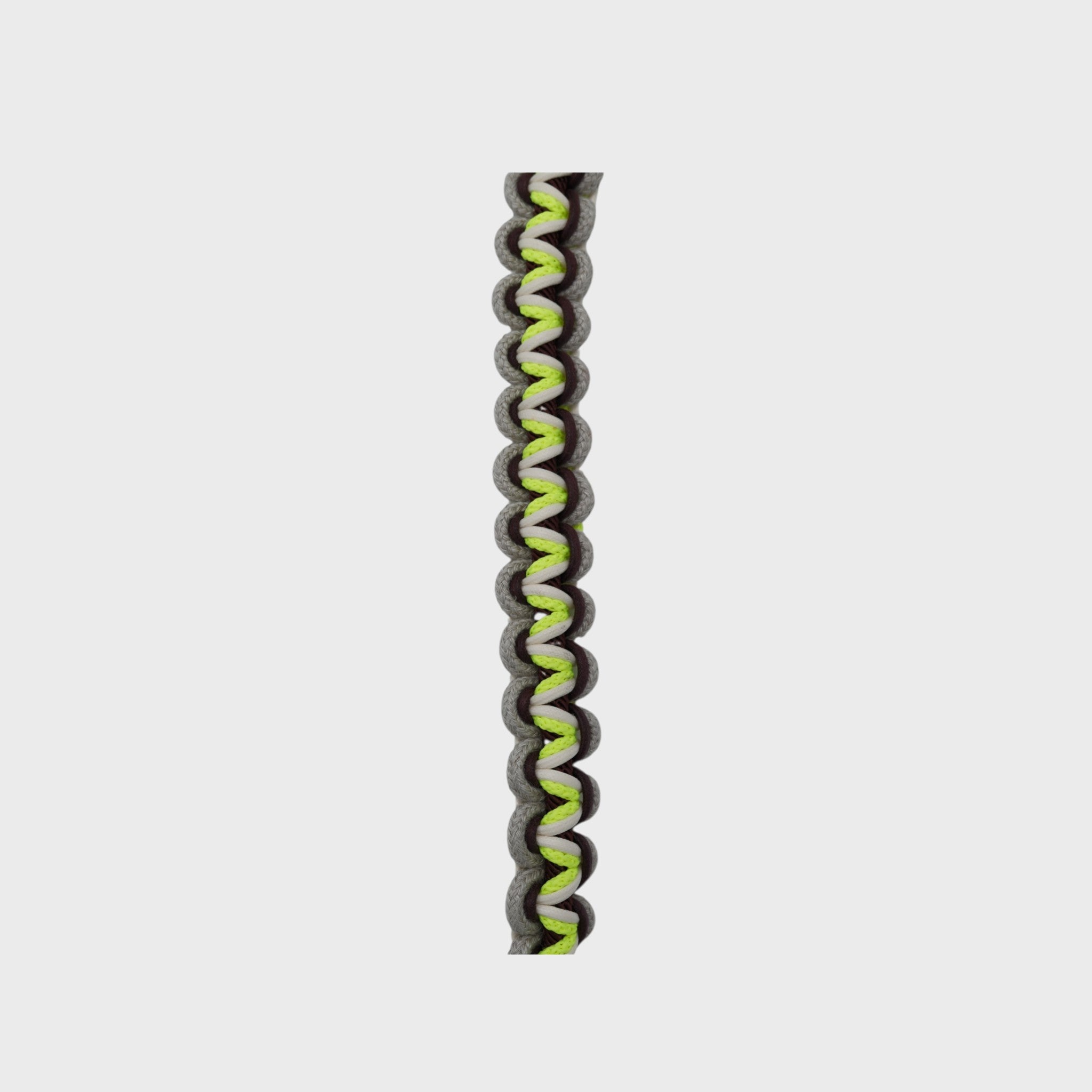 Close up of the multicolored braided macramé bag strap in neon yellow, beige, and brown shown on a light gray background.