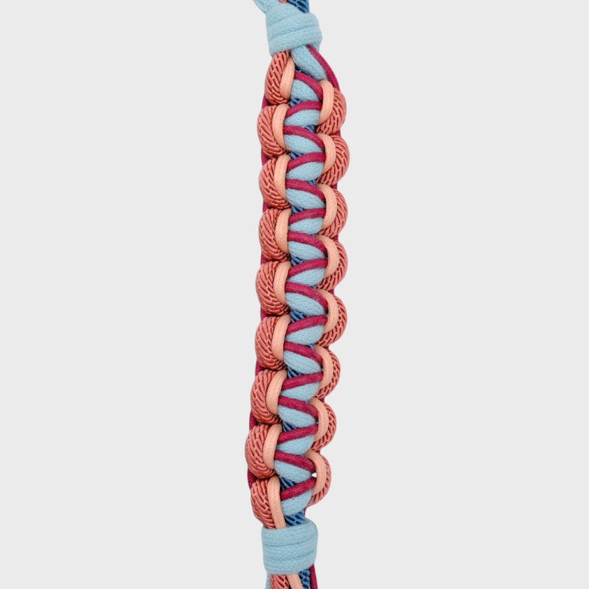 Close up of the multicolored braided macramé bag strap in light blue, soft pink, and dark blue shown on a light gray background.