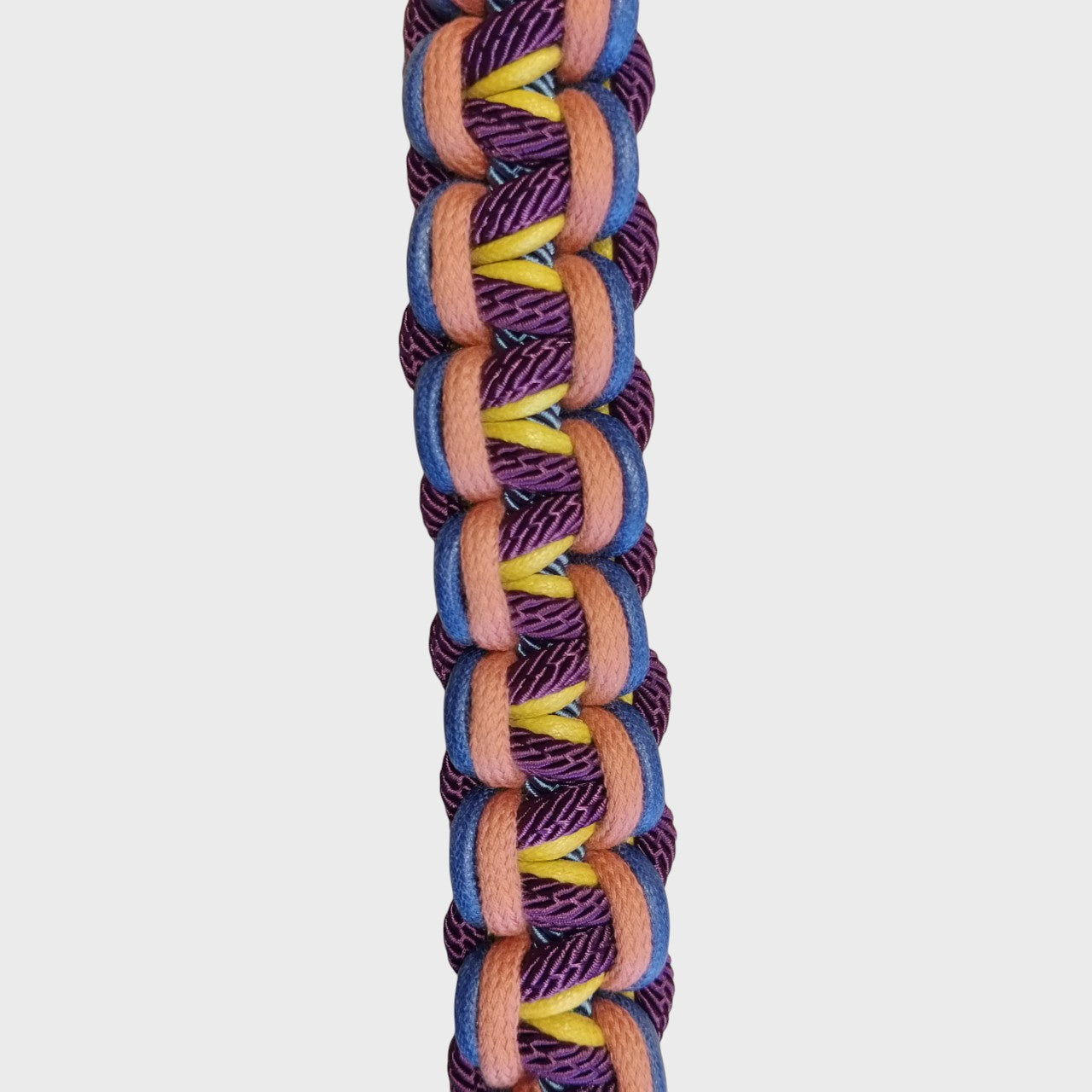 A close up of the multicolored braided macramé bag strap in bright pink, bright blue, and light blue with metal hooks on a light gray background.