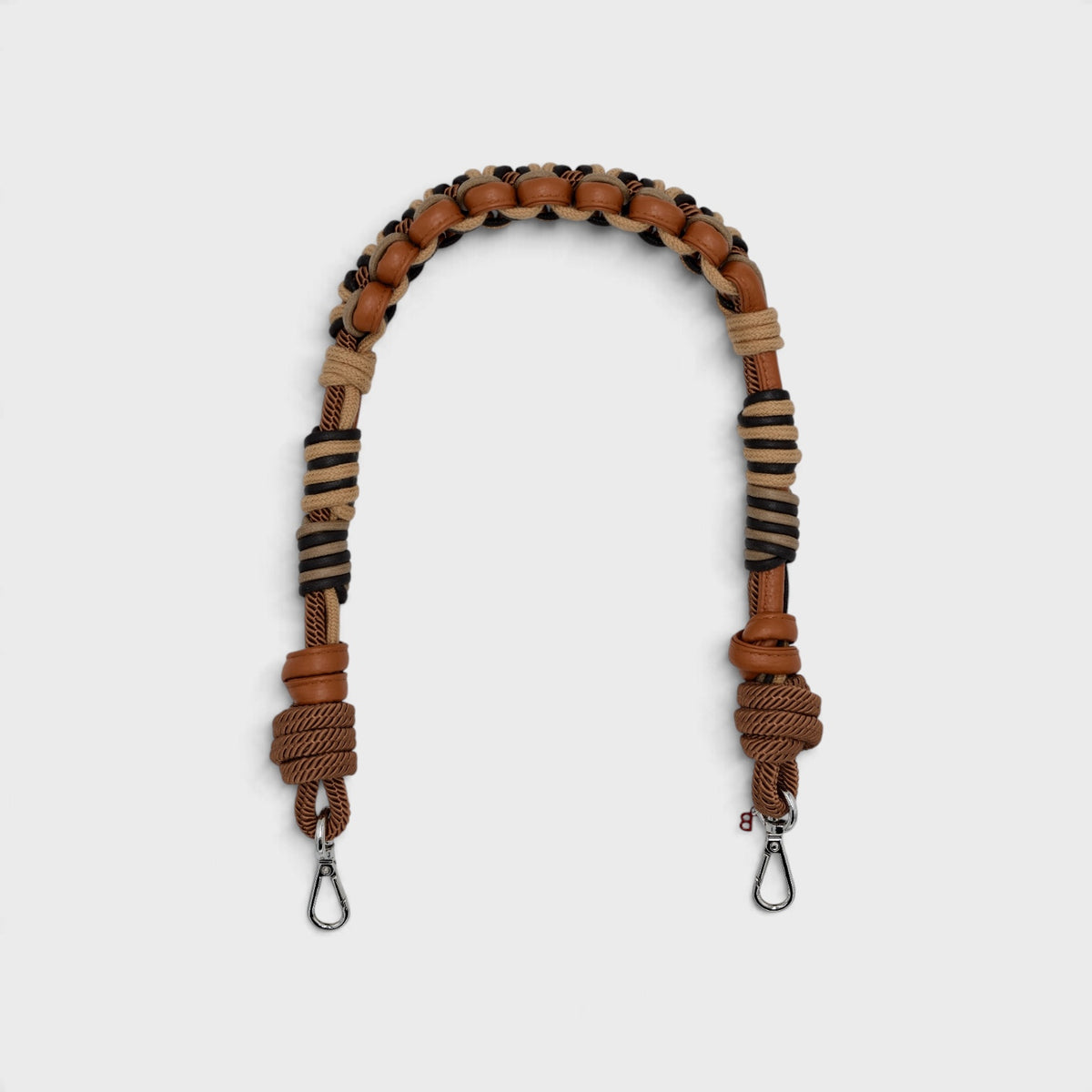 A shoulder strap with a braided loop of brown leather and tan cords,  knotted ends, and silver metal clips, shown on a light gray background.