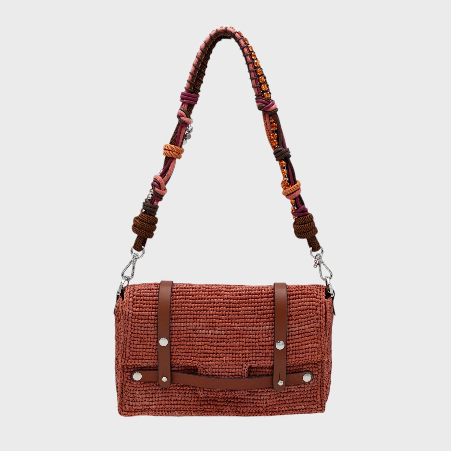 A dusty pink raffia shoulder bag with brown leather straps hanging by a colorful macramé braided strap featuring brown, pink and small beaded orange stones, set against a light gray background.