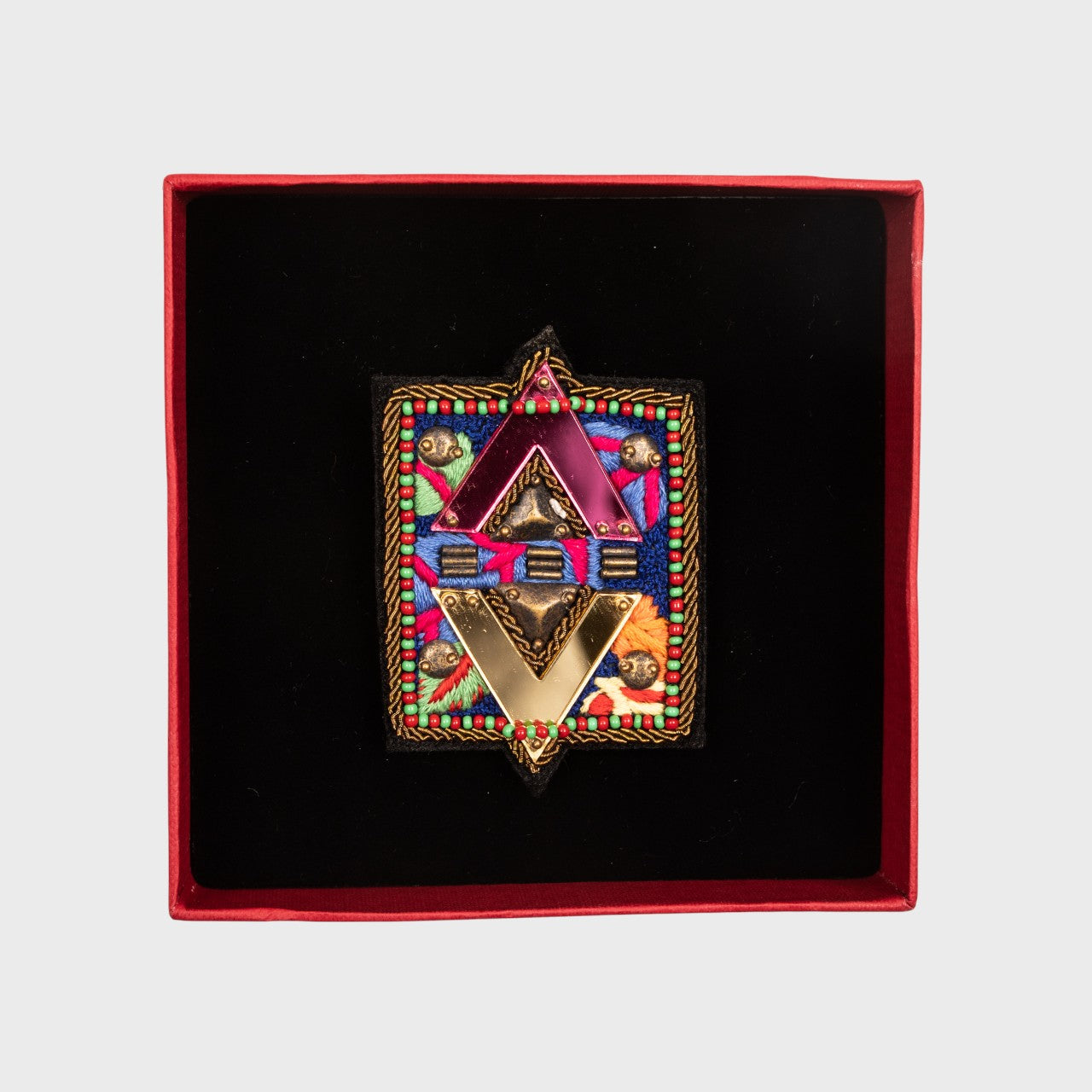 An embroidered brooch symbolizing the elements in a box. 