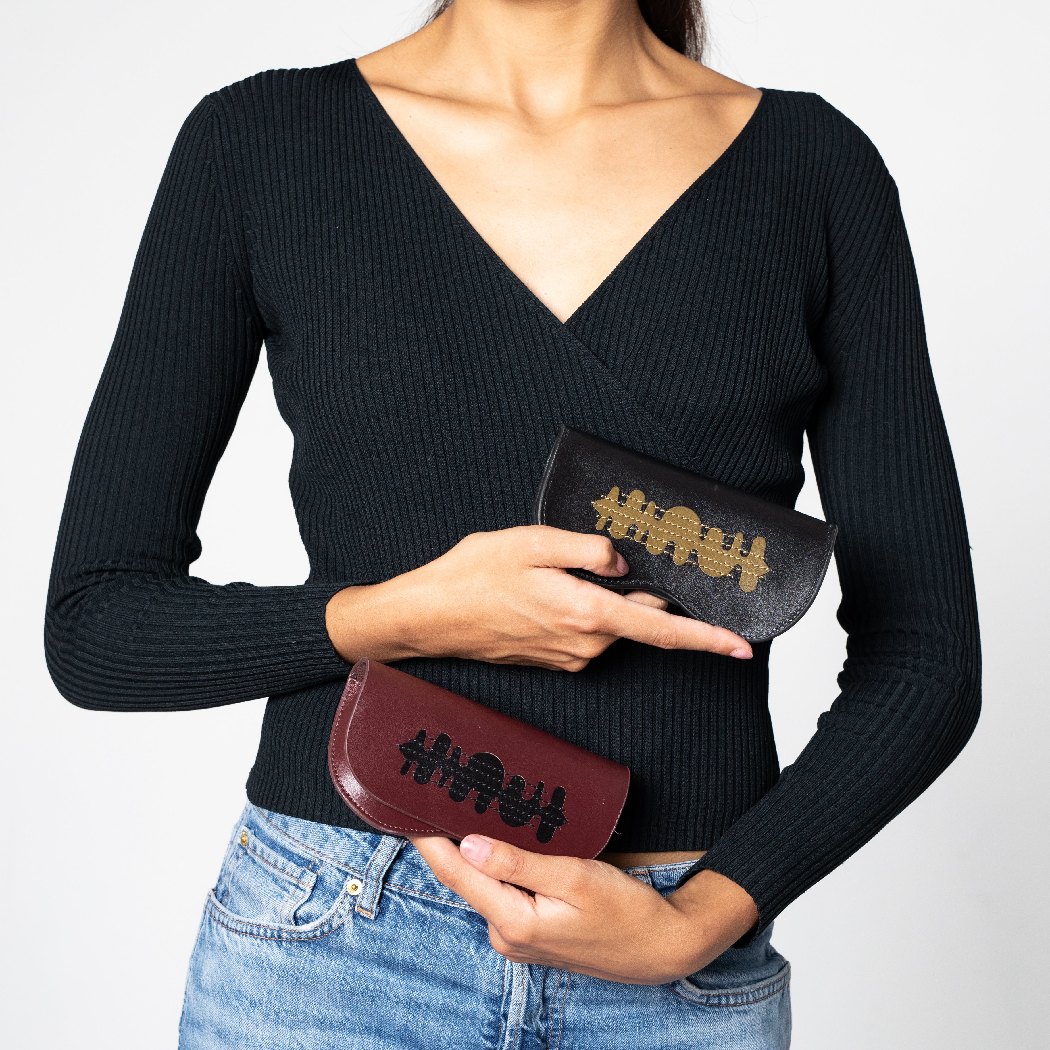 A model holding two glasses cases including the burgundy fern one with black details. 