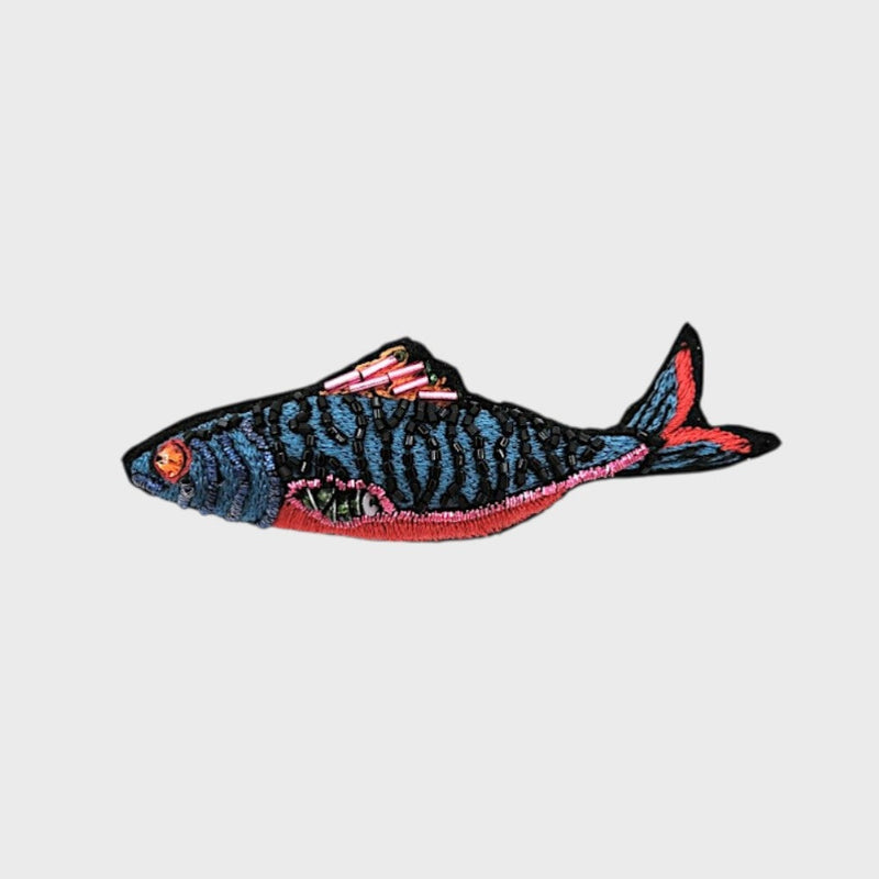 An embroidered blue fish brooch with pink, red and black details. 