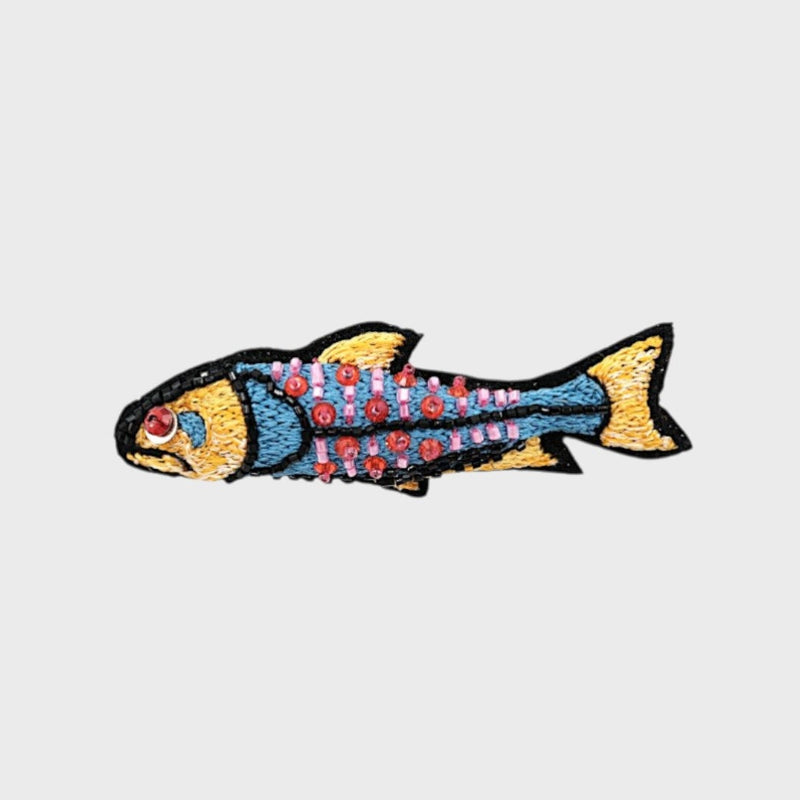 An embroidered blue fish brooch with yellow, red and pink details. 