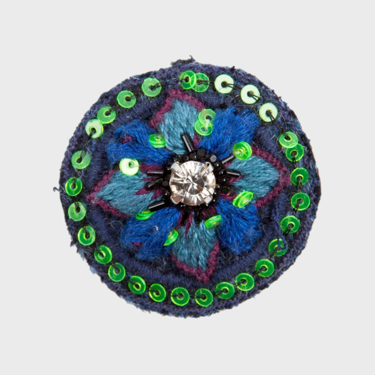 An embroidered brooch representing a blue flower with green and blue details. 