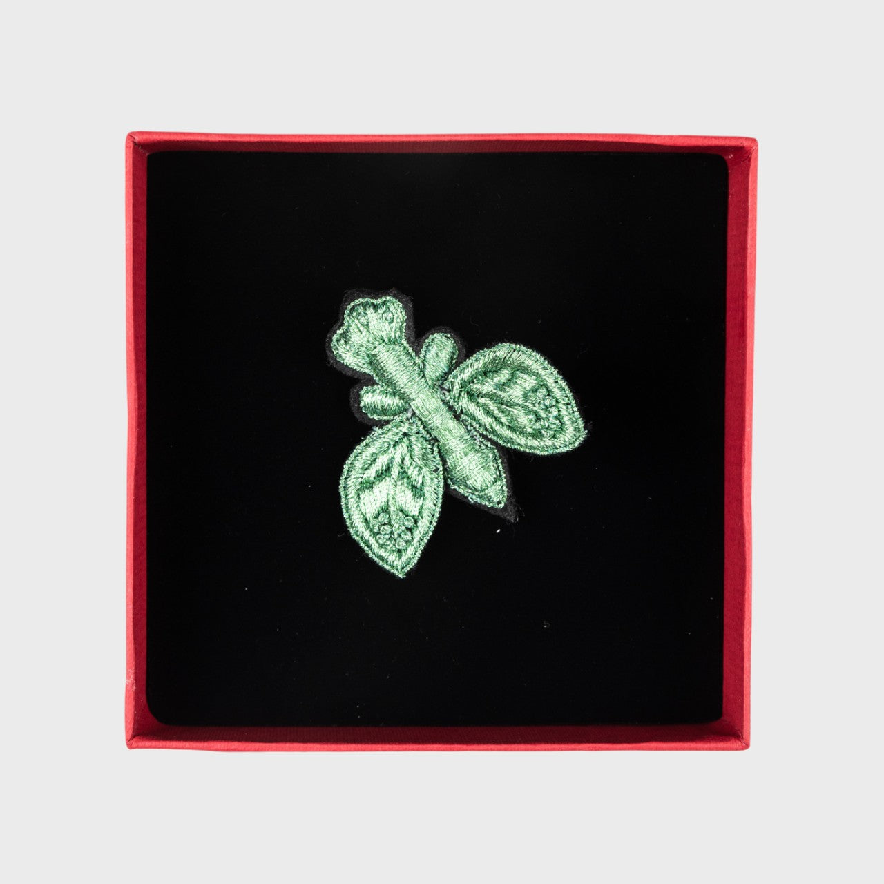An embroidered brooch of a green fly in a box. 