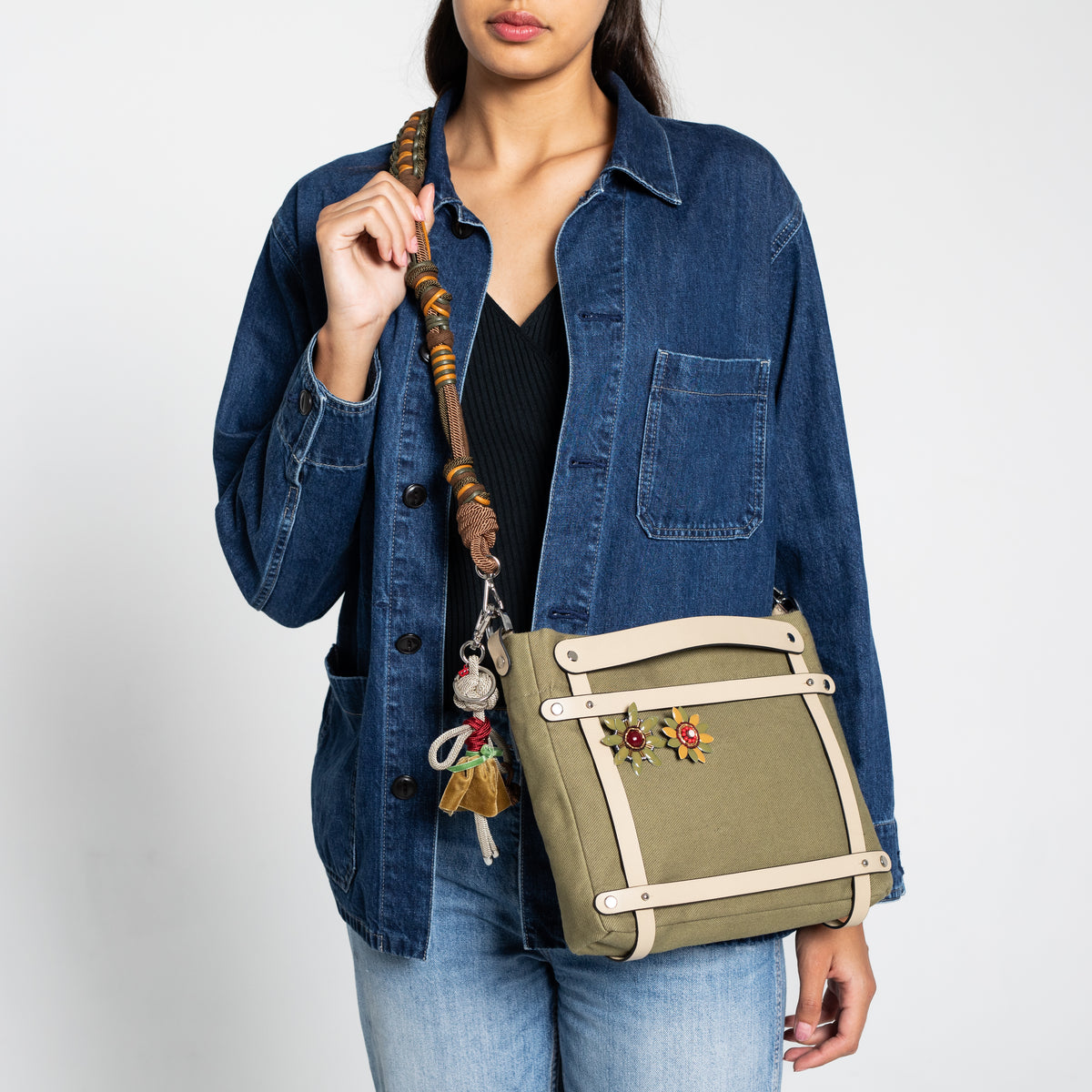 Person holding a green handbag with a cross body brown and green macramé bag strap against a plain background