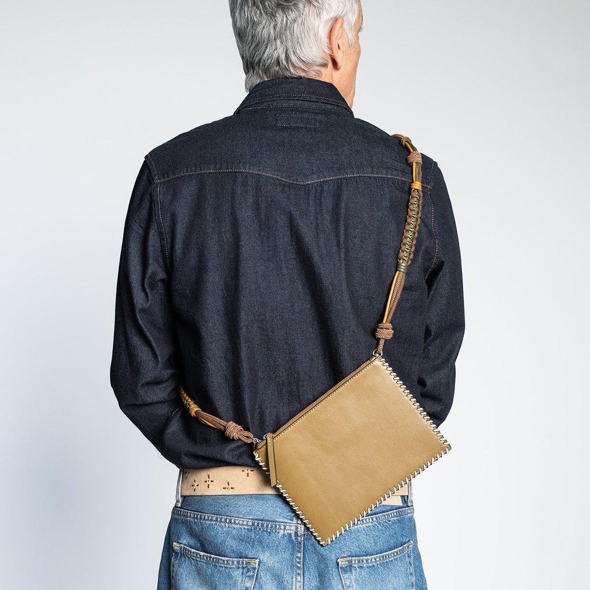 A man carrying cross body thanks to a macramé strap a rectanguar bag. 