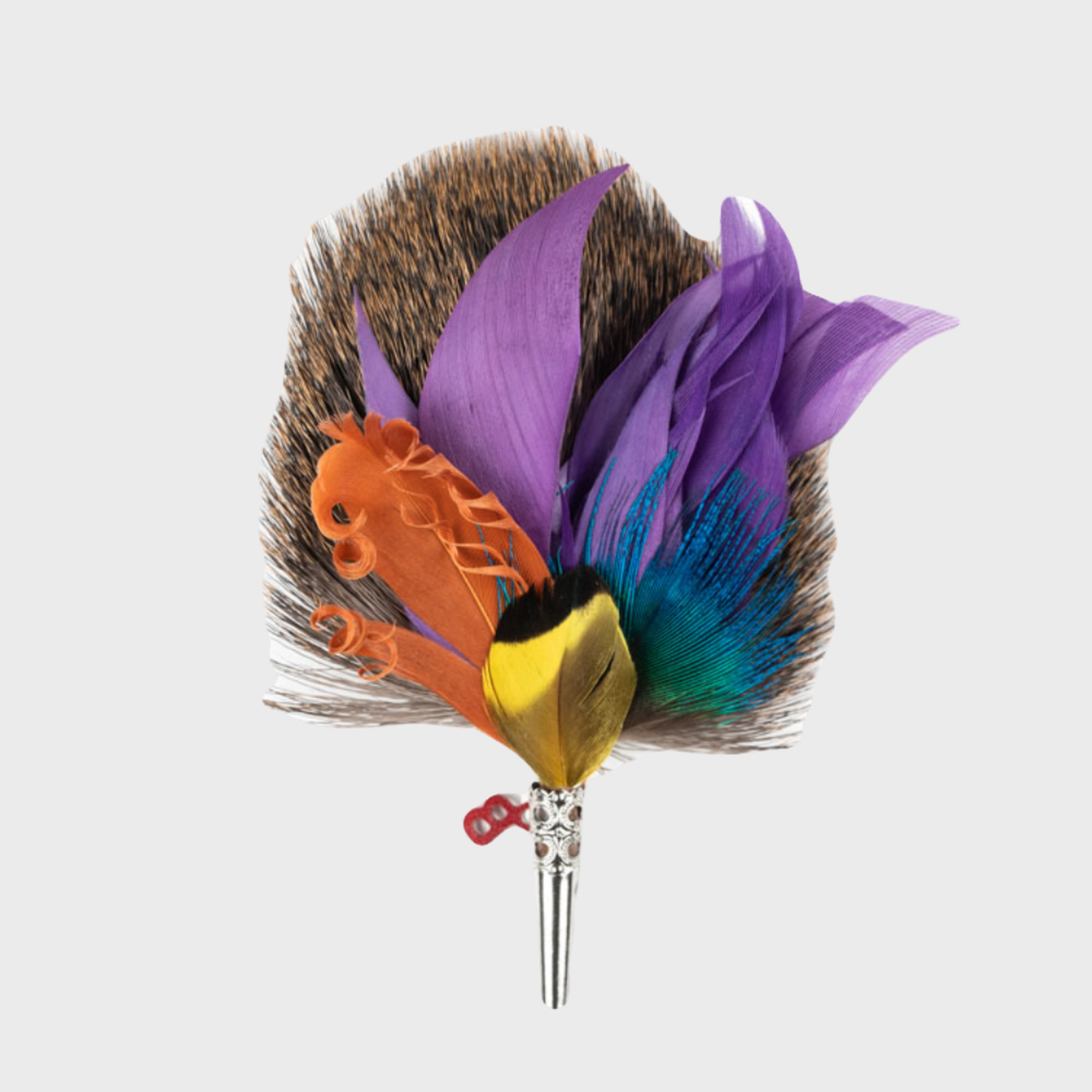 A feather brooch with a combination of natural and colored feathers, attached to a metal stake, presented against a white background.