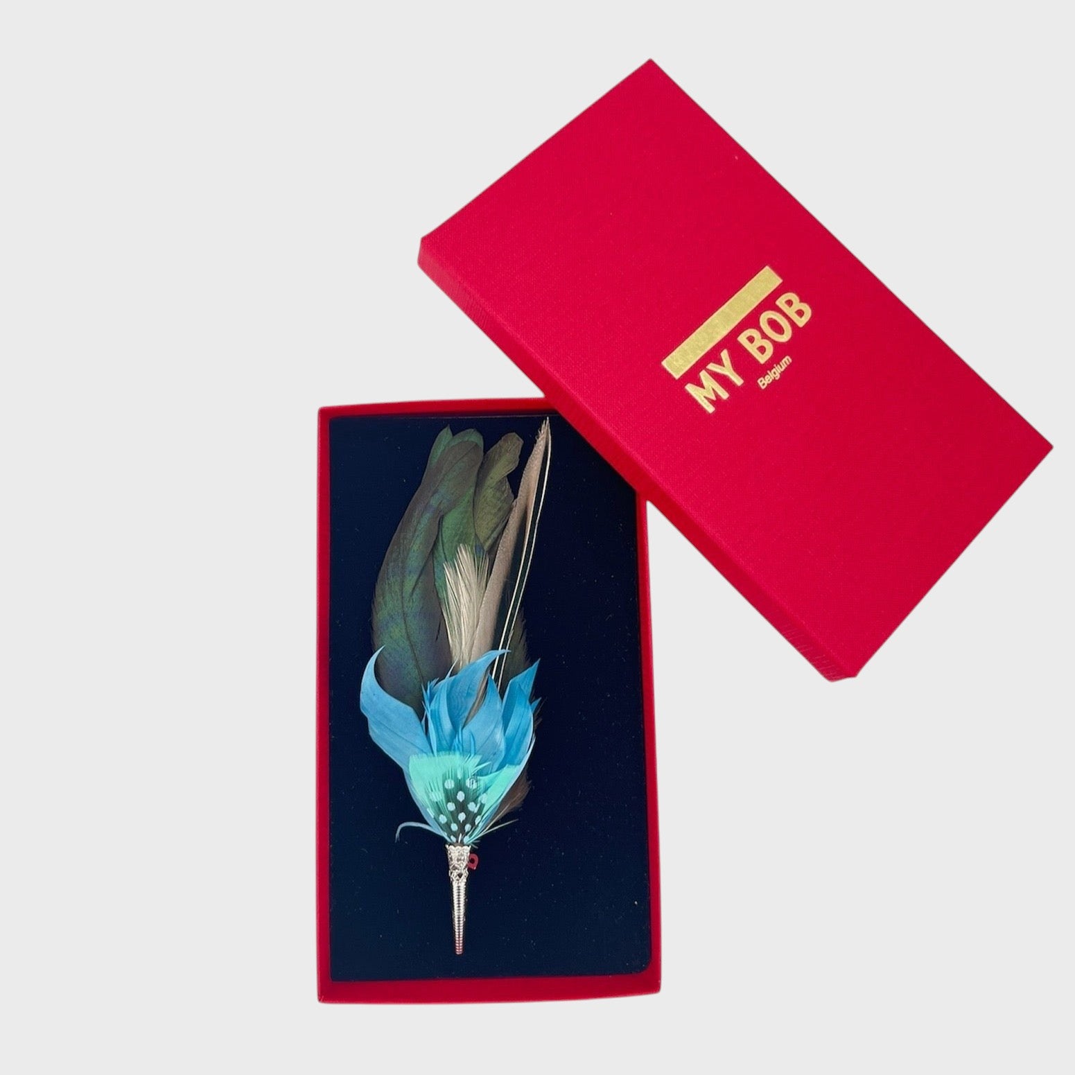 Large Blue and green feather brooch in a box on a light gray background