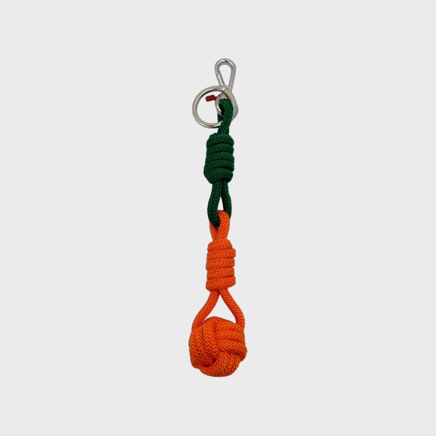 A macramé keychain representing a ball inspired by sailors knots. The straight upper part is green and the ball part is orange. 