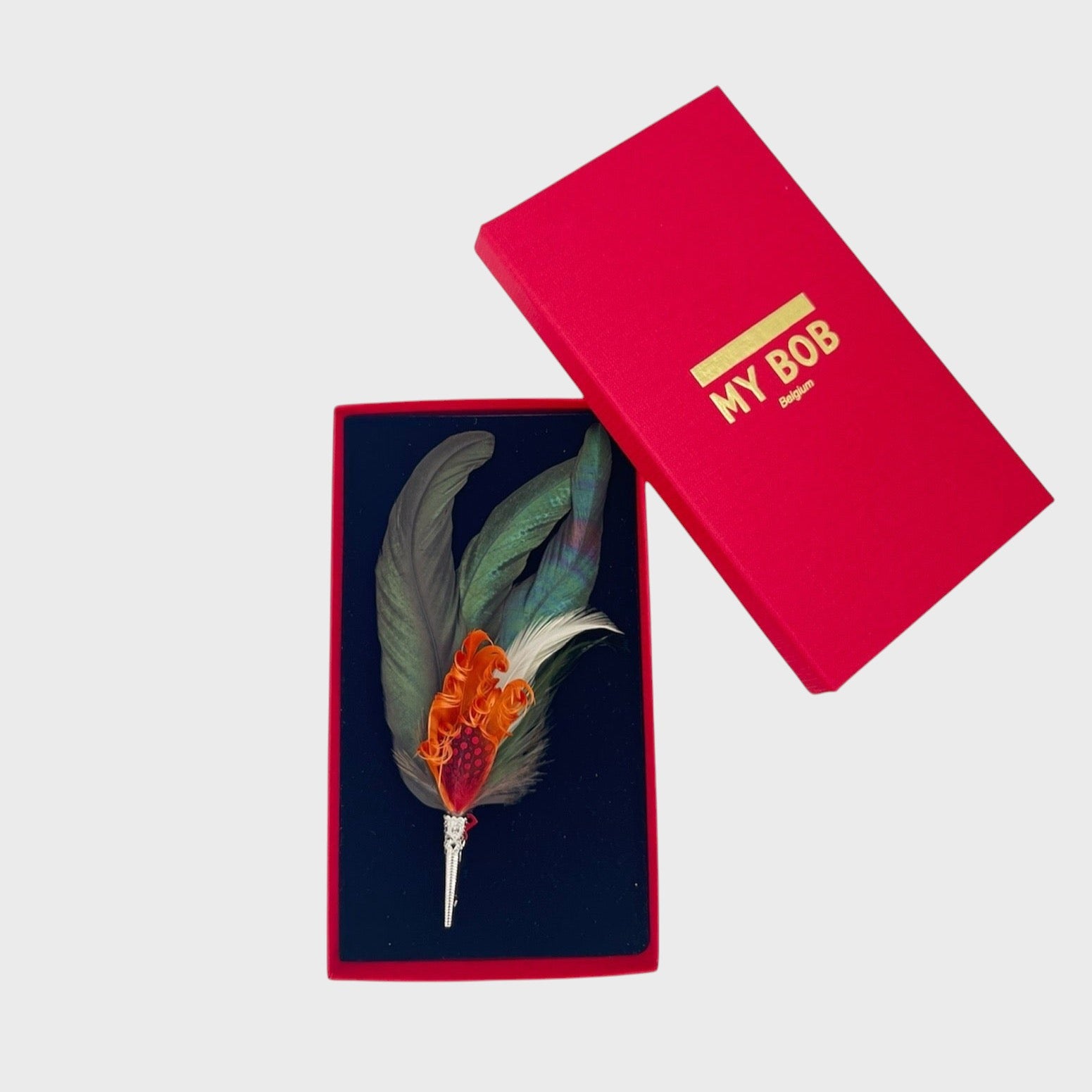 Large green and red-orange feather brooch in a box on a light gray background