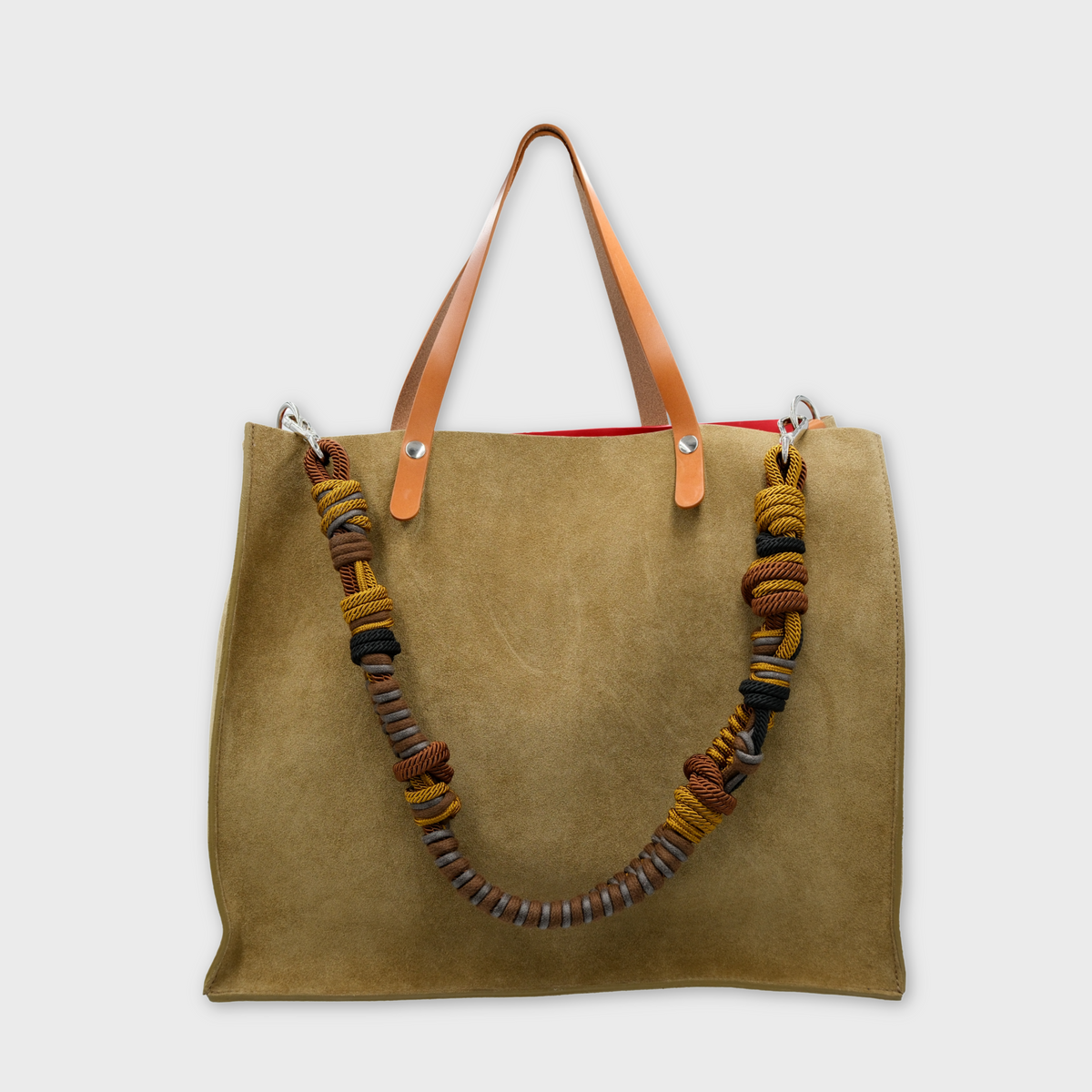 A large green suede tote bag with light brown leather shoulder straps and a thick braided multicolor macrame strap, shown against a light gray background.