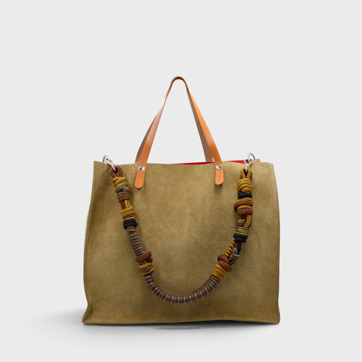 A large green suede tote bag with light brown leather shoulder straps and a thick braided multicolor macrame strap, shown against a light gray background.