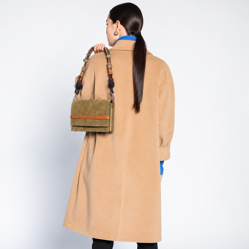A woman carrying a green suede flapbag by a bag strap. 