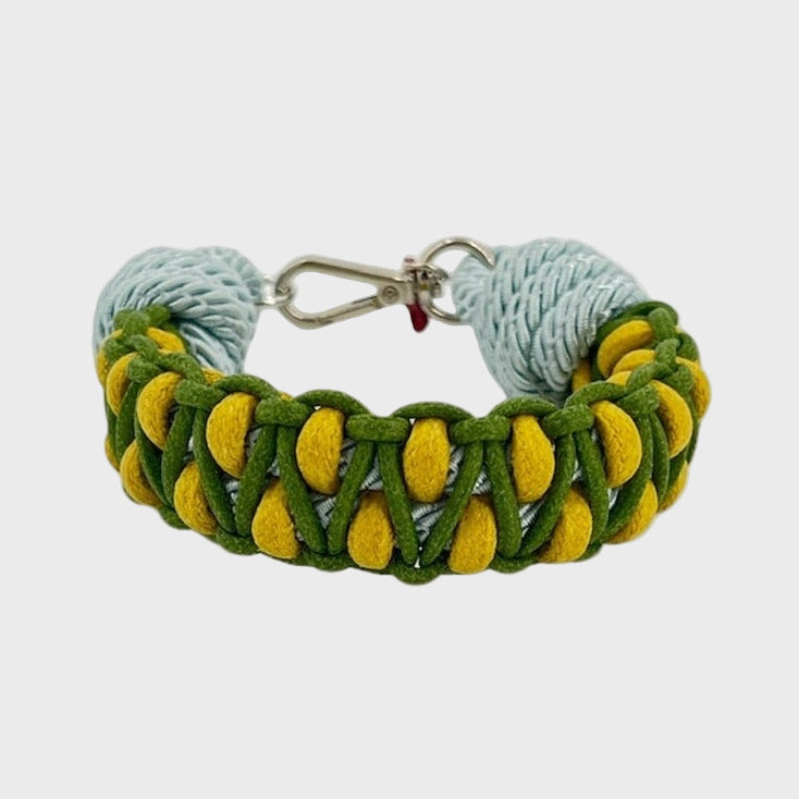 A braided macramé bracelet with shades of green, yellow and light blue. It ends and a silver clasp, shown on a light gray background.