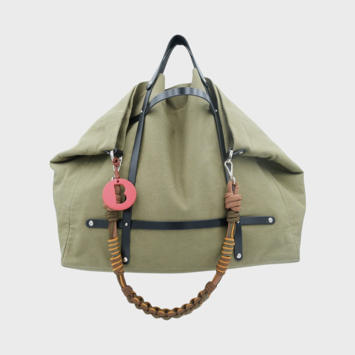 Green cotton bag with black leather straps and  a green woven bag strap on a light gray background