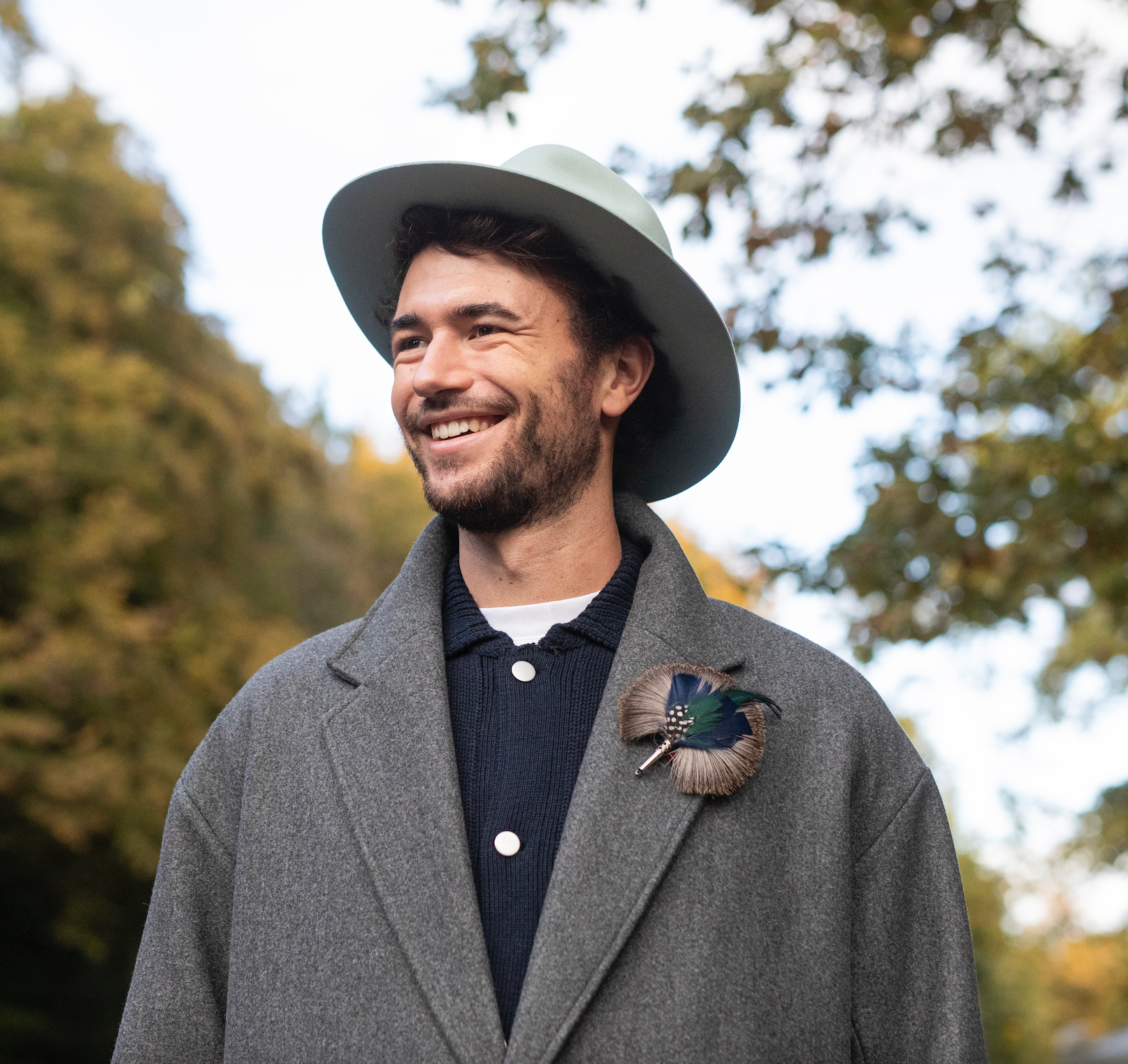 A model wearing on his coat the round green, grey and blue feather brooch. 