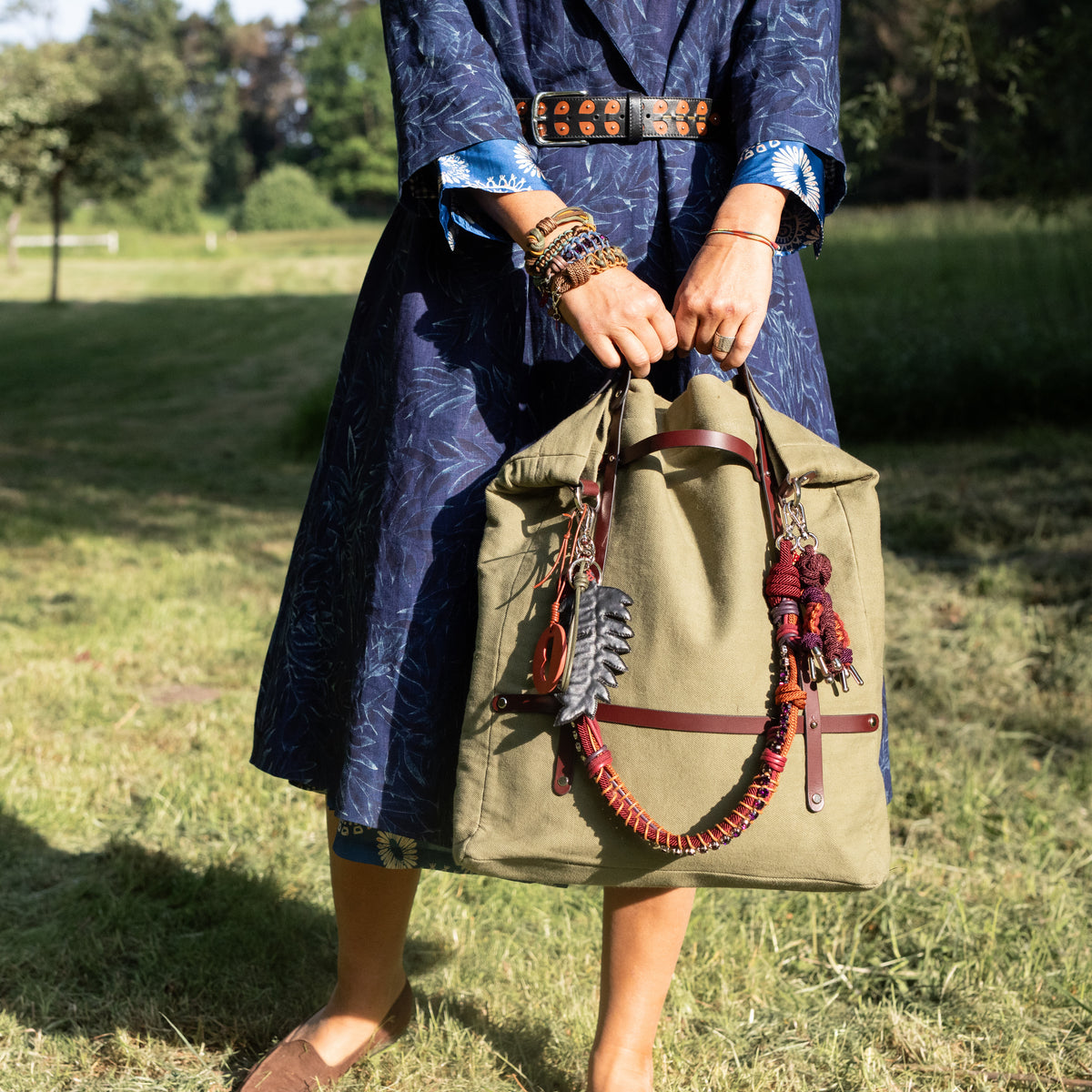Person holding a green bag with a burgundy macramé strap with purple rhinestones in a natural setting