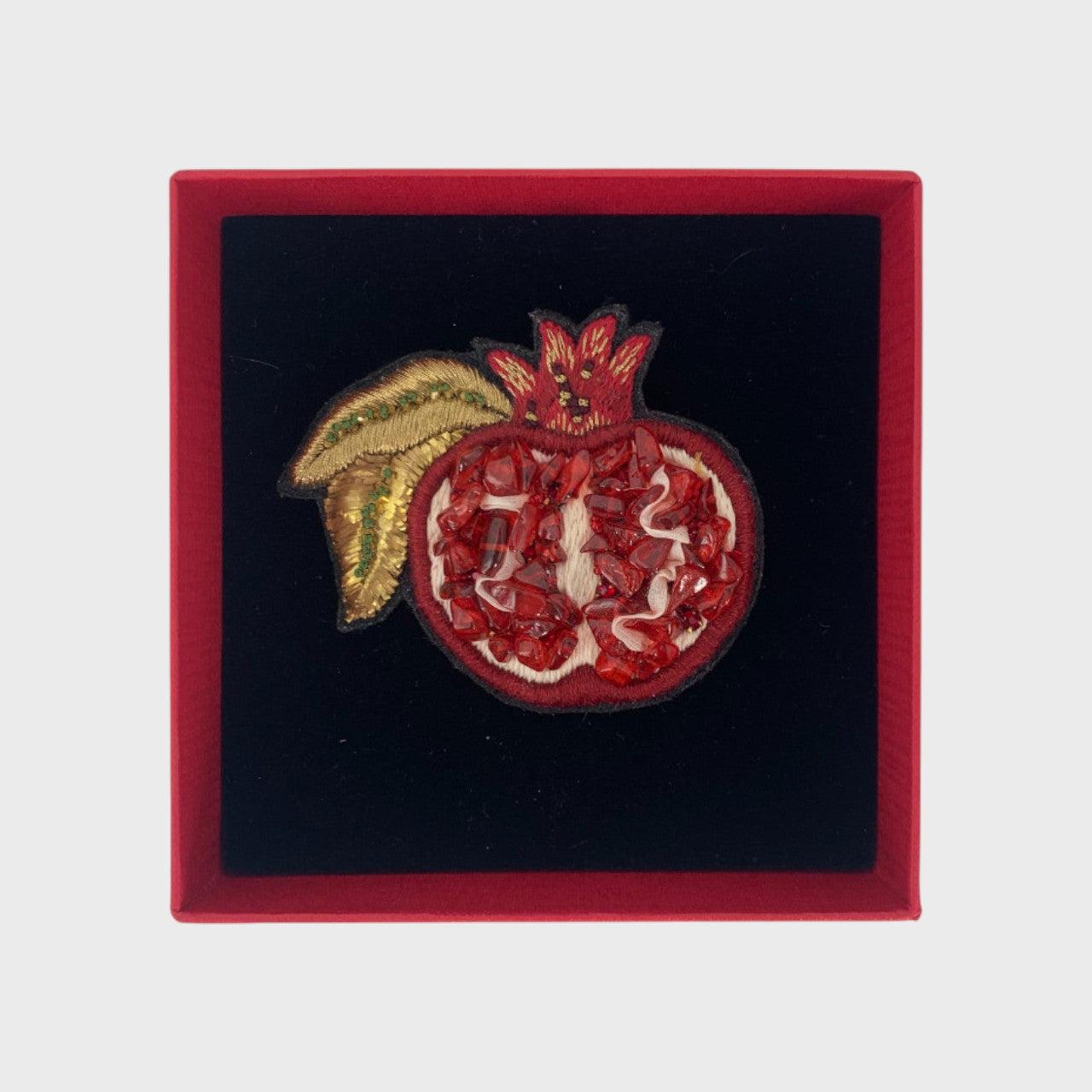 An embroidered brooch representing a grenade in a box. 